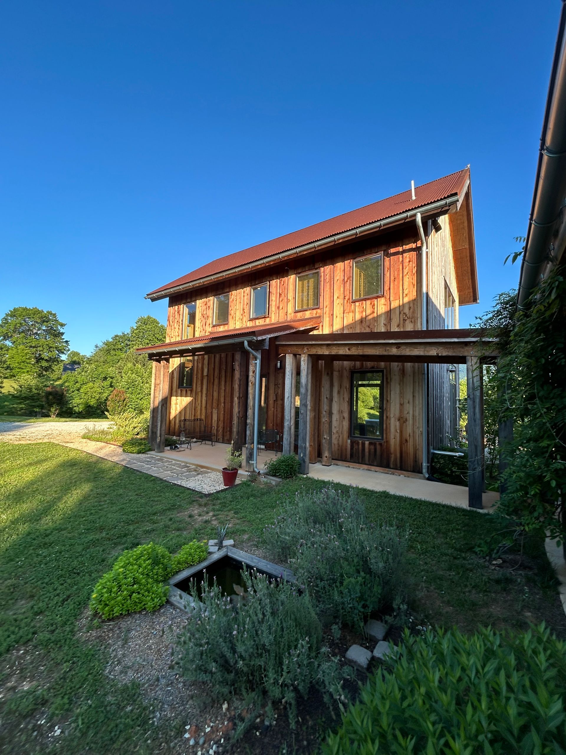 A large wooden house with a red roof is surrounded by grass and trees.