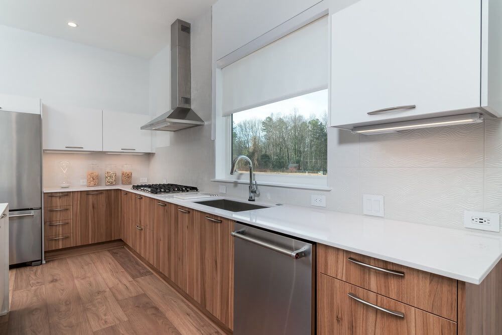 A kitchen with wooden cabinets , white counter tops , stainless steel appliances and a large window.