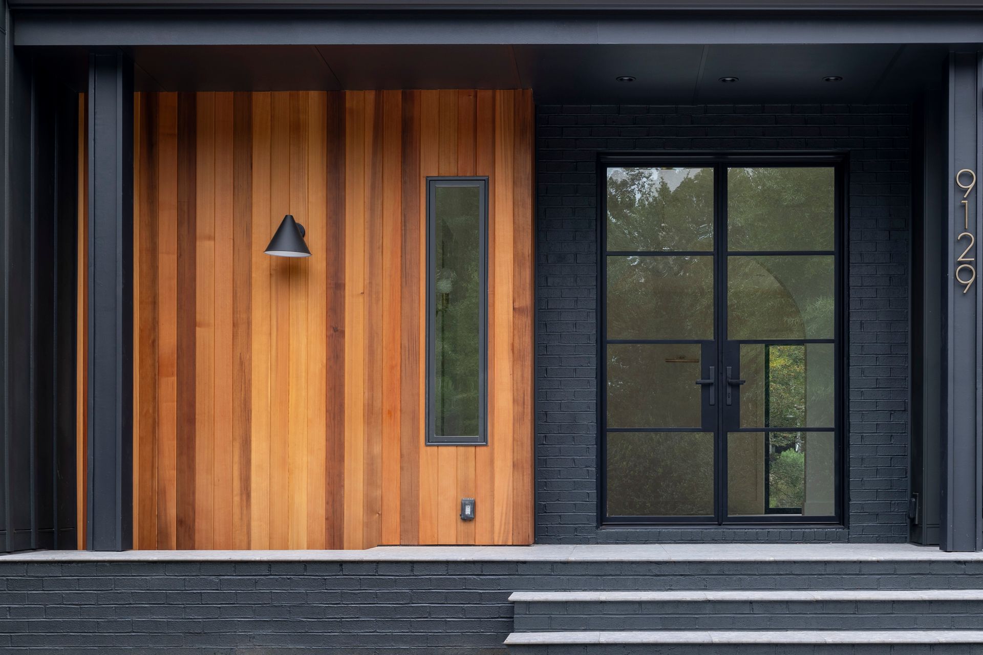 The front door of a house with a wooden door and black windows