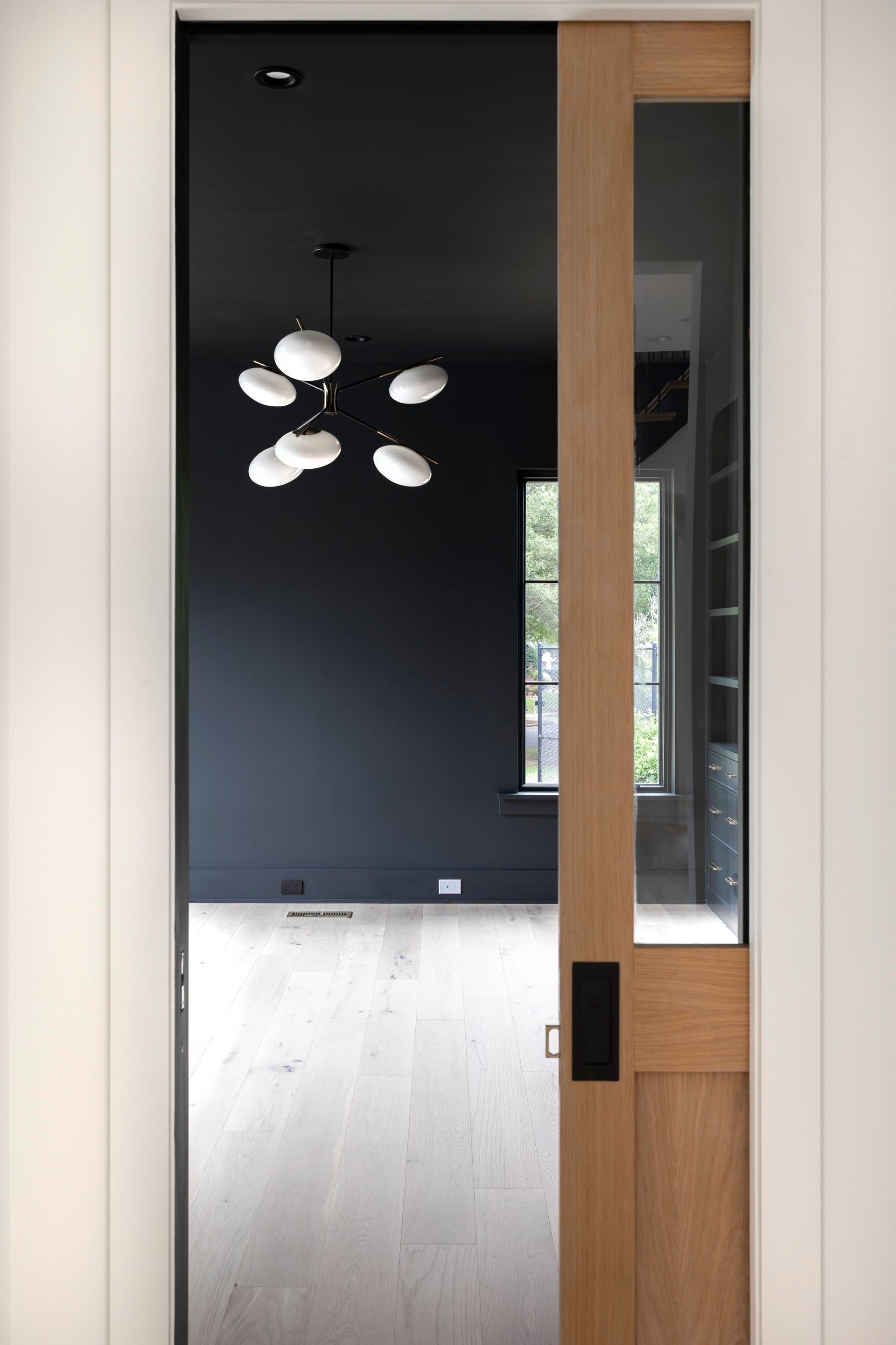 A wooden door is open to a dark room with a chandelier hanging from the ceiling.