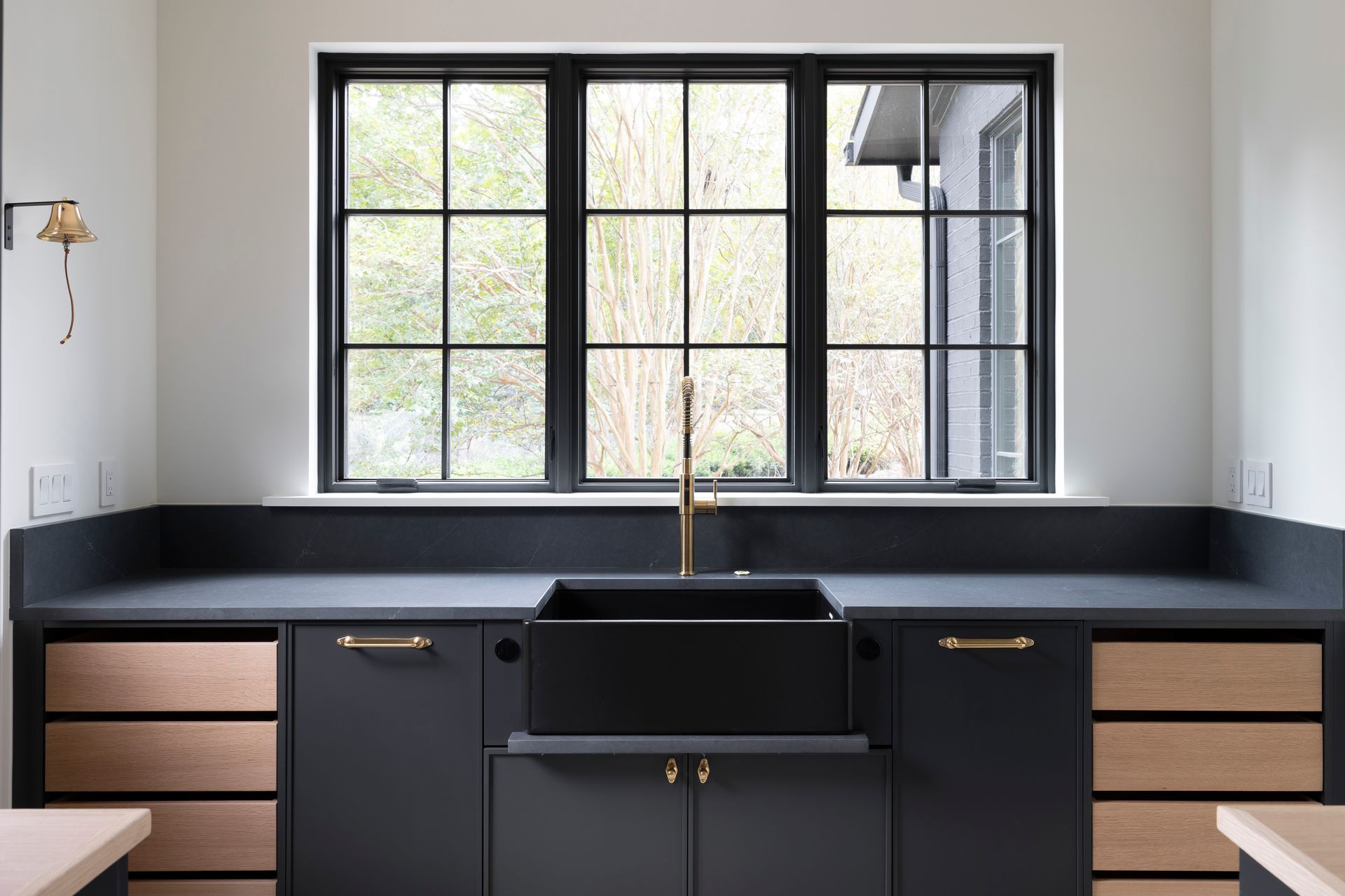 A kitchen with black cabinets and a black sink under a window.