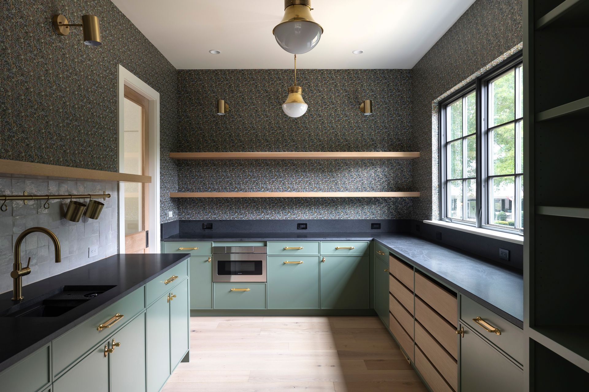 A kitchen with green cabinets , black counter tops , and a sink.