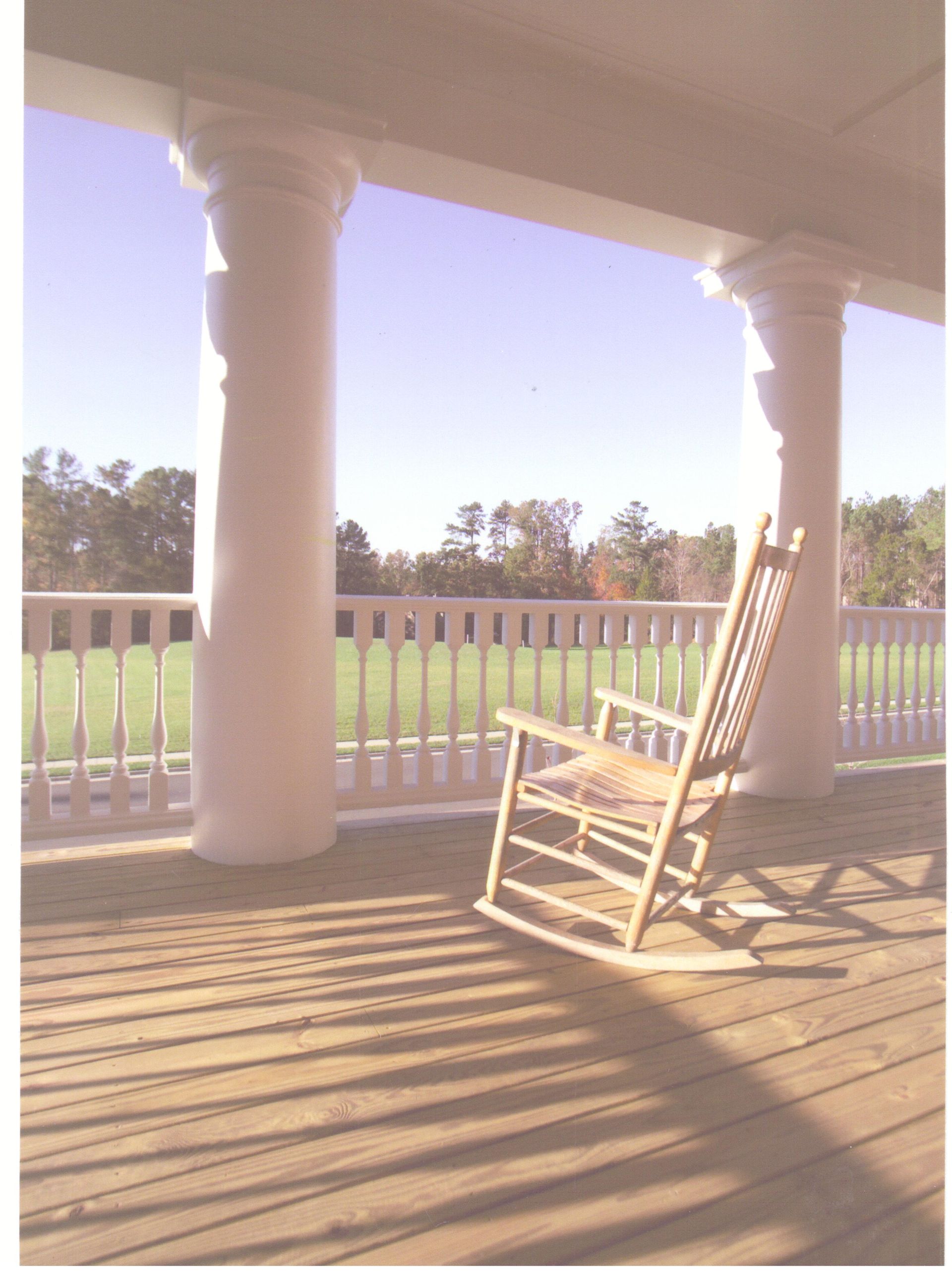 A rocking chair on a porch with a view of a field