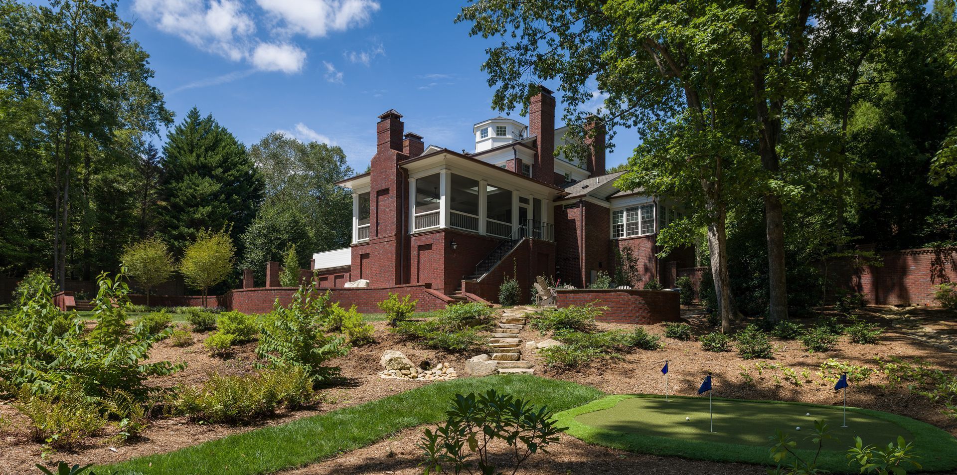 a large brick house with a large porch is surrounded by trees and bushes .