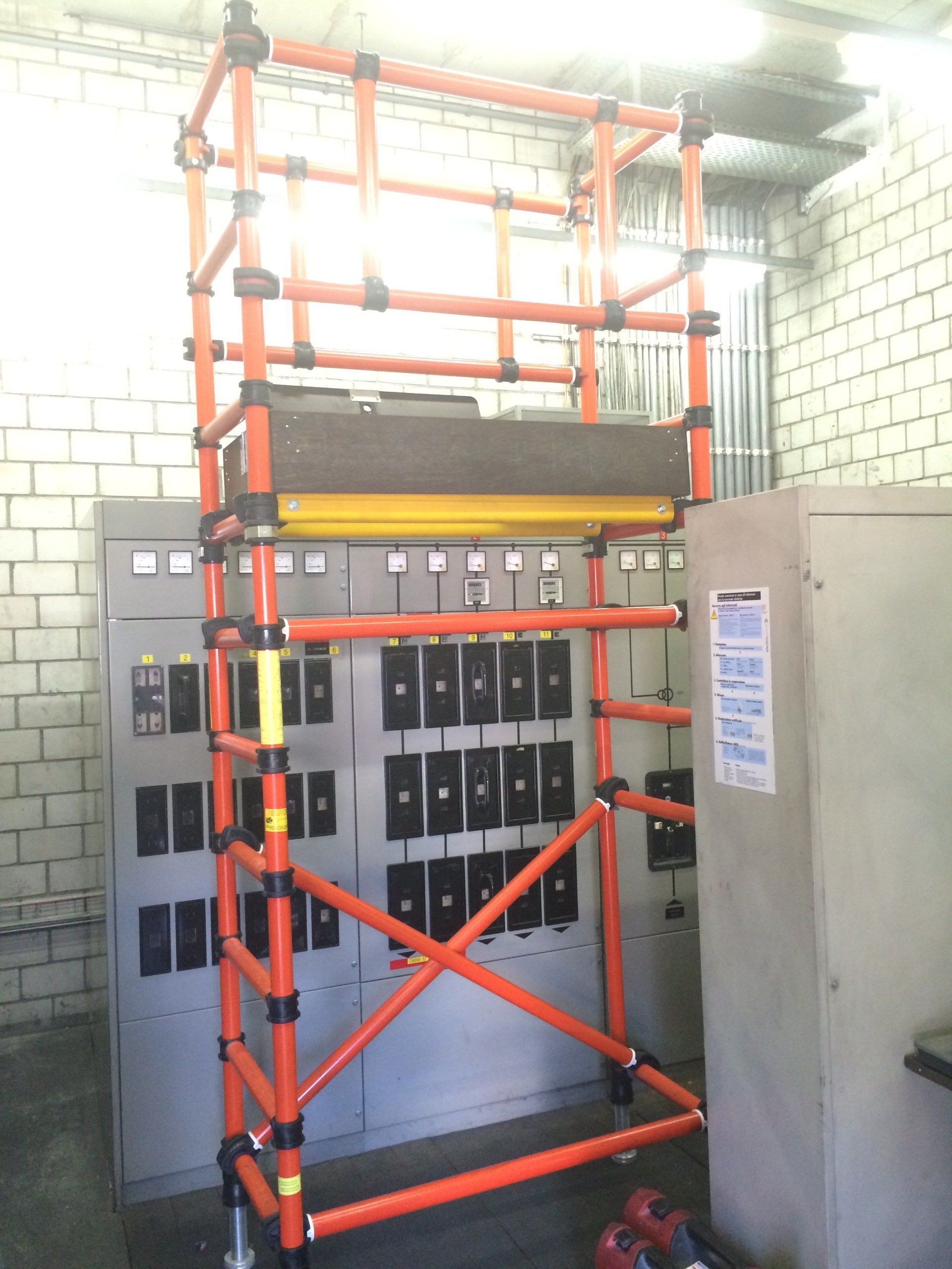 An orange scaffolding is in front of a wall of electrical boxes