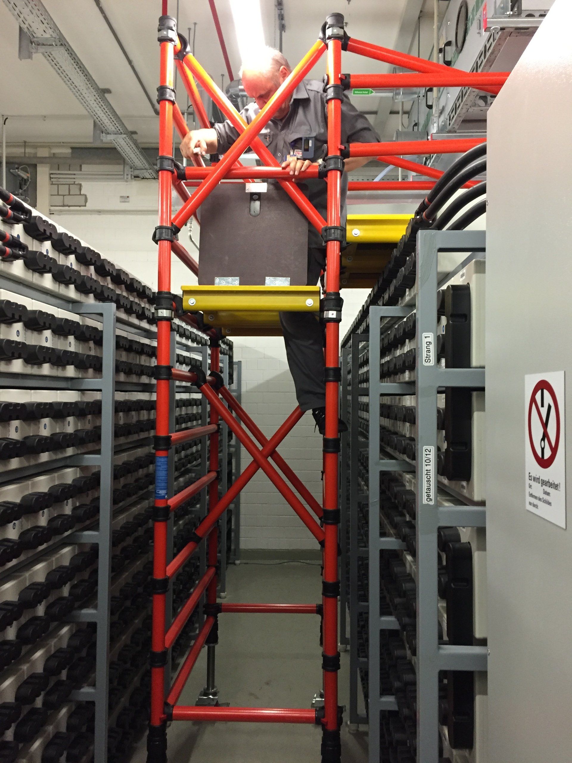 A man is standing on a red scaffolding in a warehouse
