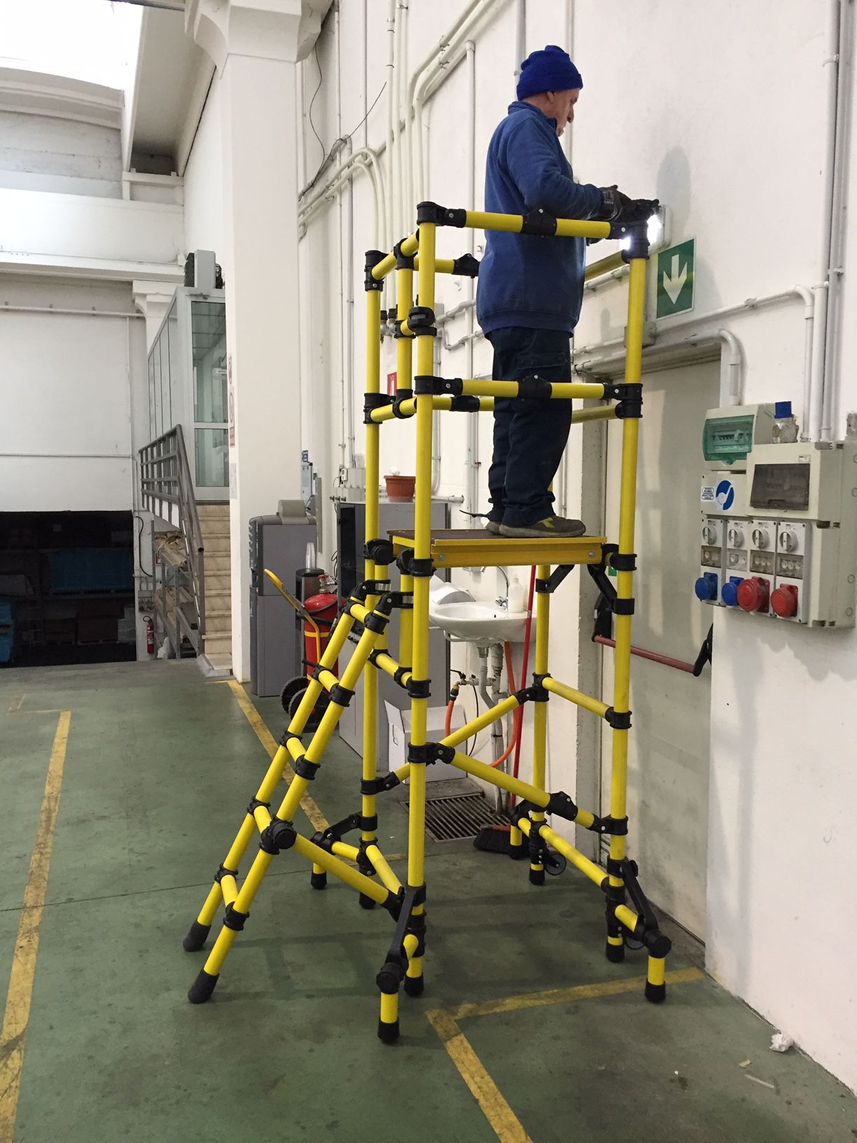 A man is standing on a yellow ladder in front of a green exit sign