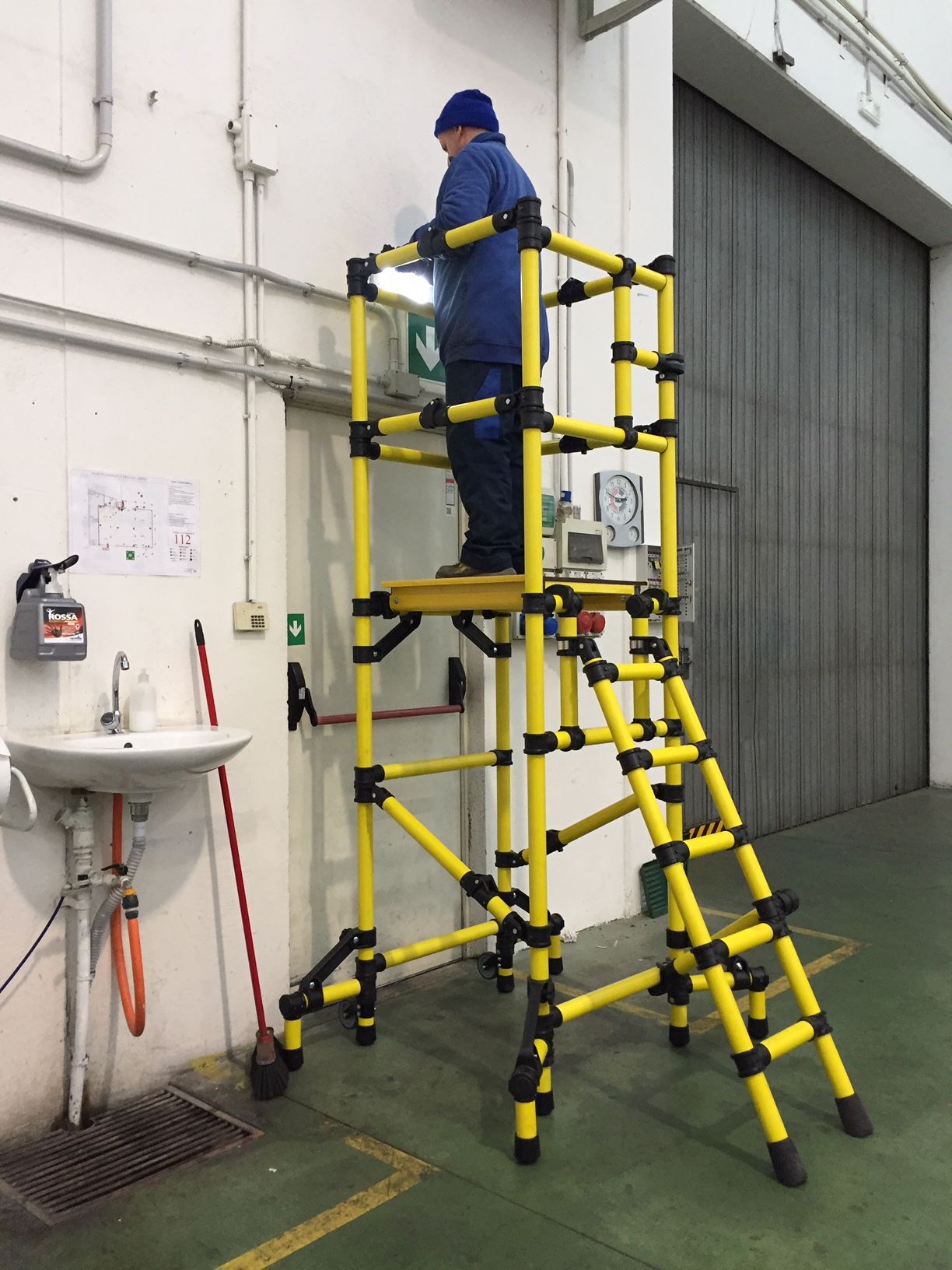 A man is standing on a yellow ladder in a warehouse.