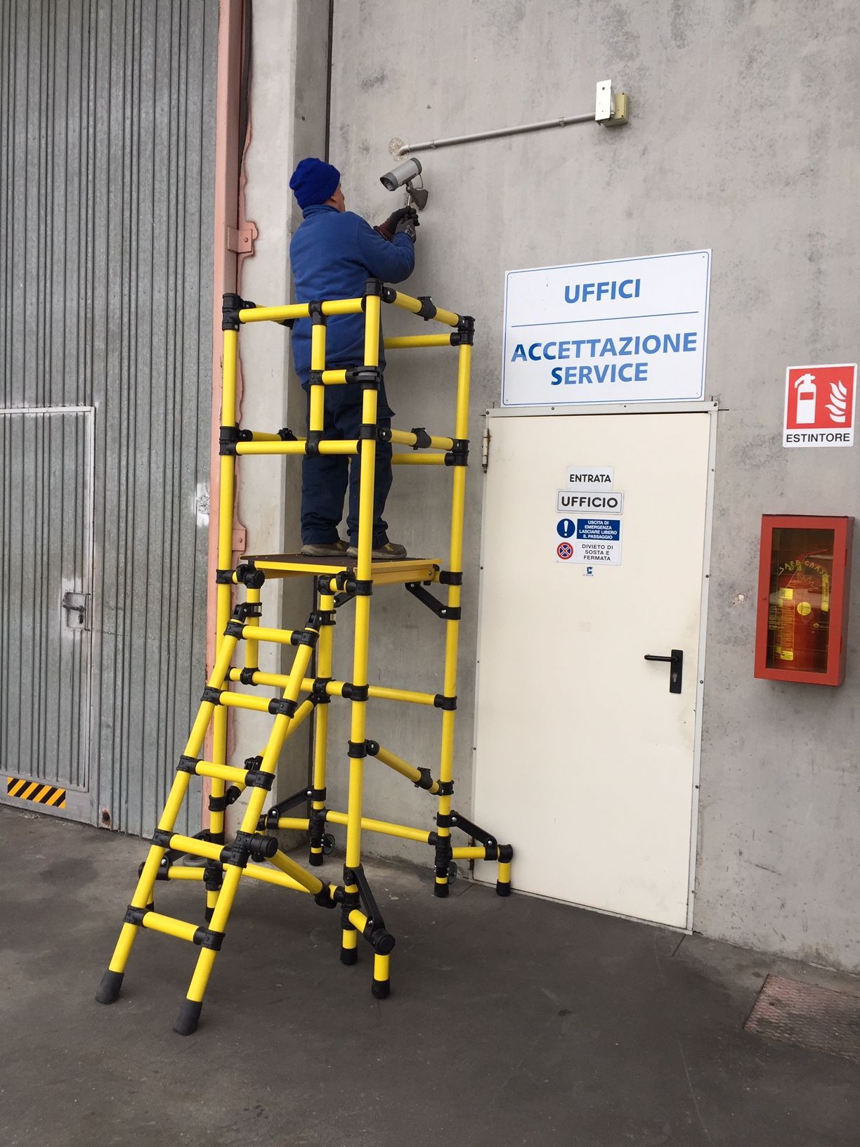 A man is standing on a yellow ladder in front of a sign that says uffici