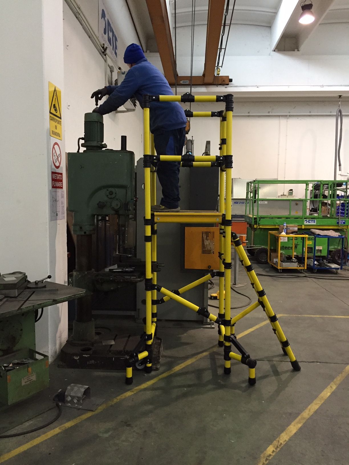 A man is standing on a yellow ladder in a factory