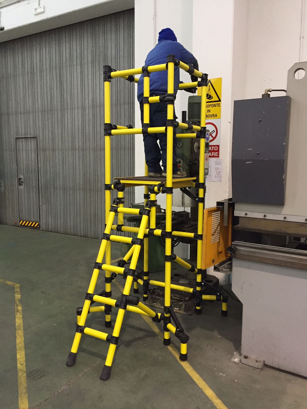 A man is standing on a yellow ladder in a warehouse
