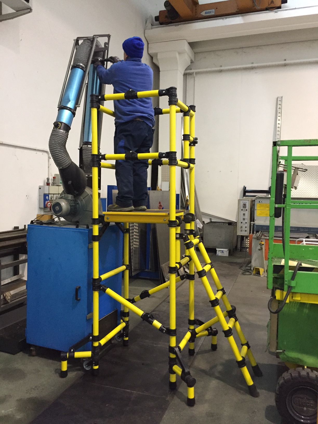 A man is standing on a yellow ladder in a factory