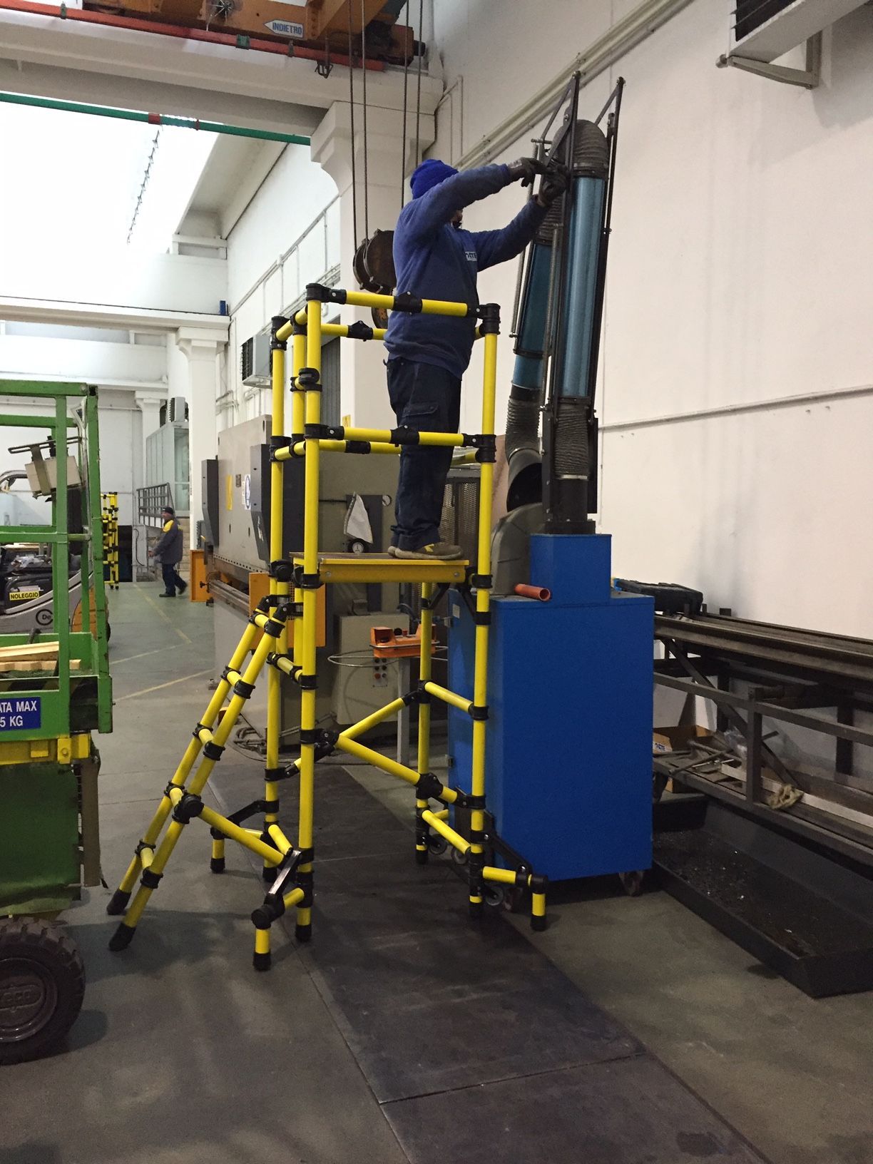 A man is standing on a yellow ladder in a factory