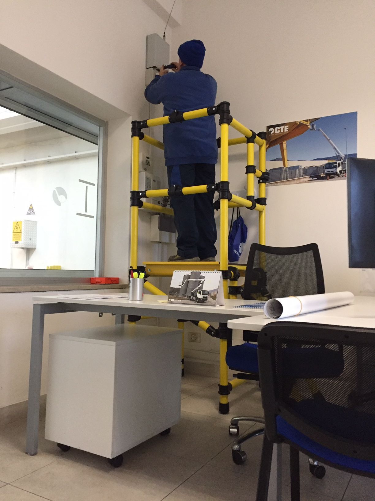 A man is standing on a yellow ladder in an office
