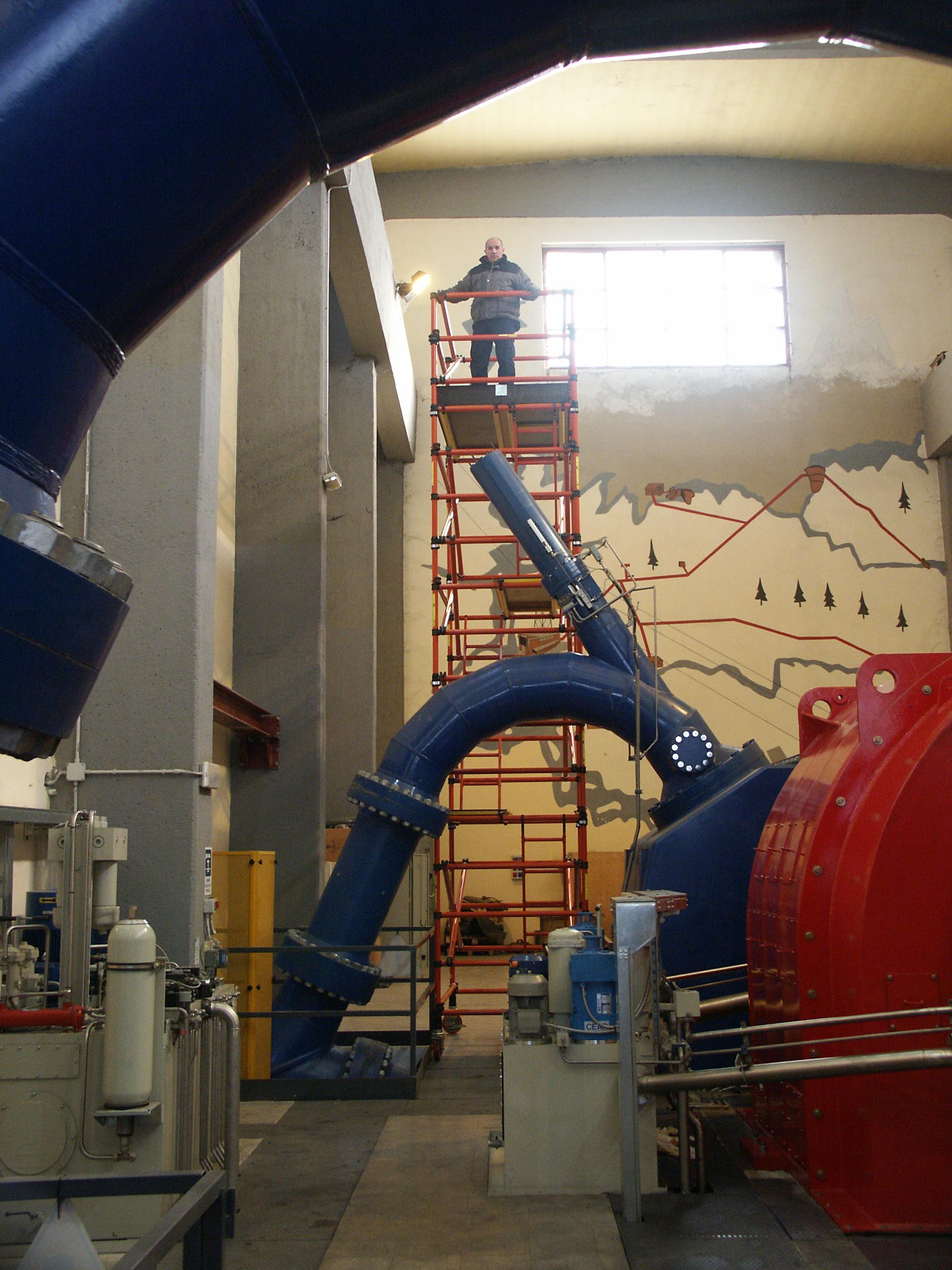 A man is standing on a scaffolding in a room with pipes