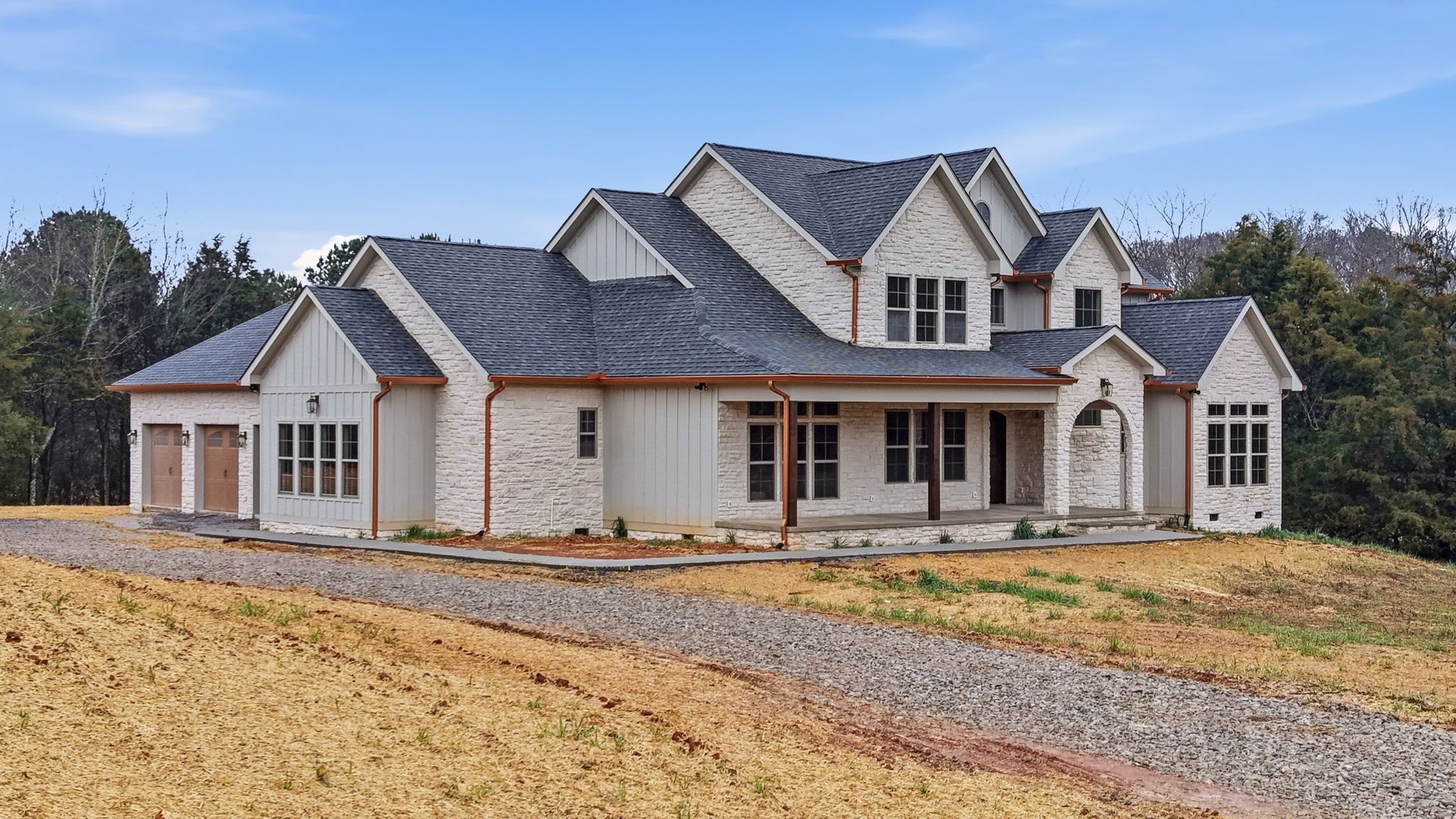 Large, light brick house with multiple gables and a covered porch. A gravel driveway leads to the front.