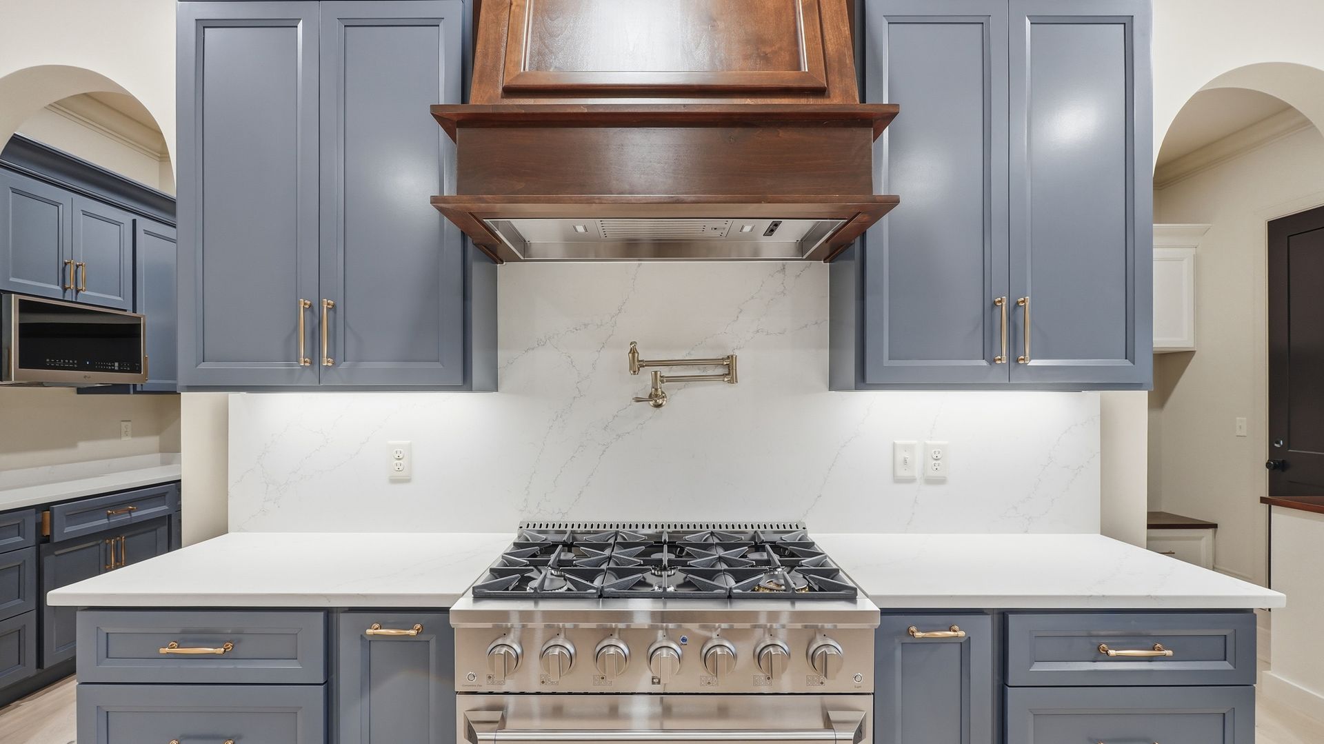Kitchen with gray cabinets, white countertops, stainless steel stove, and wood range hood.