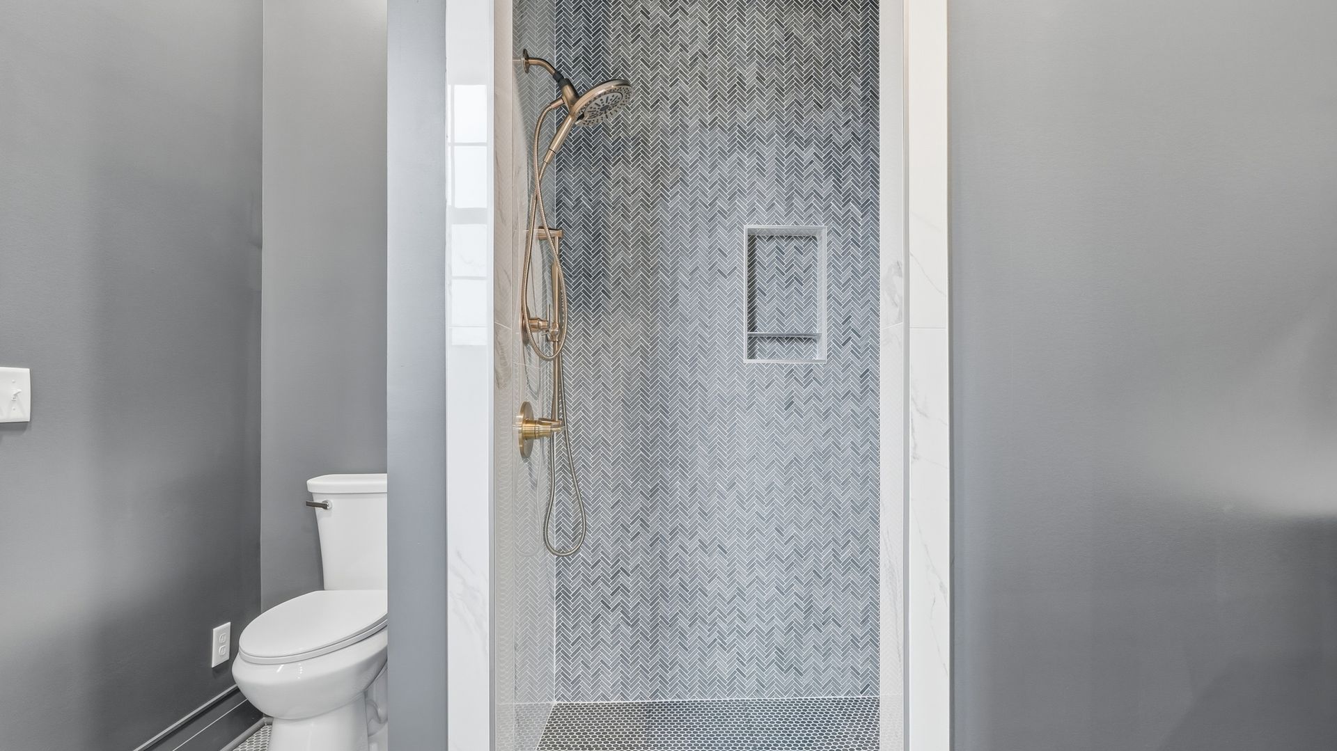 Bathroom with gray walls, white toilet, and a walk-in shower with textured gray walls and gold shower head.