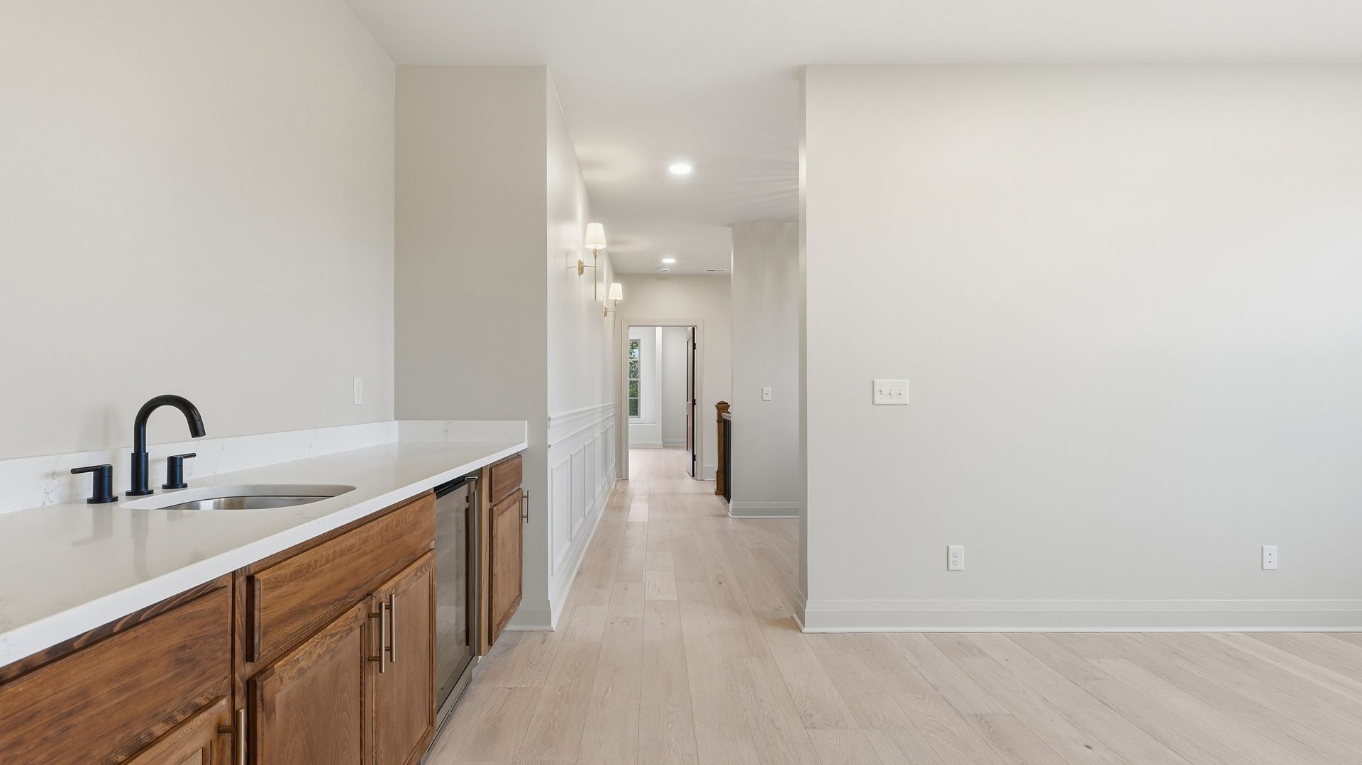 Hallway with white walls, light wood floors, and built-in bar with black faucet.