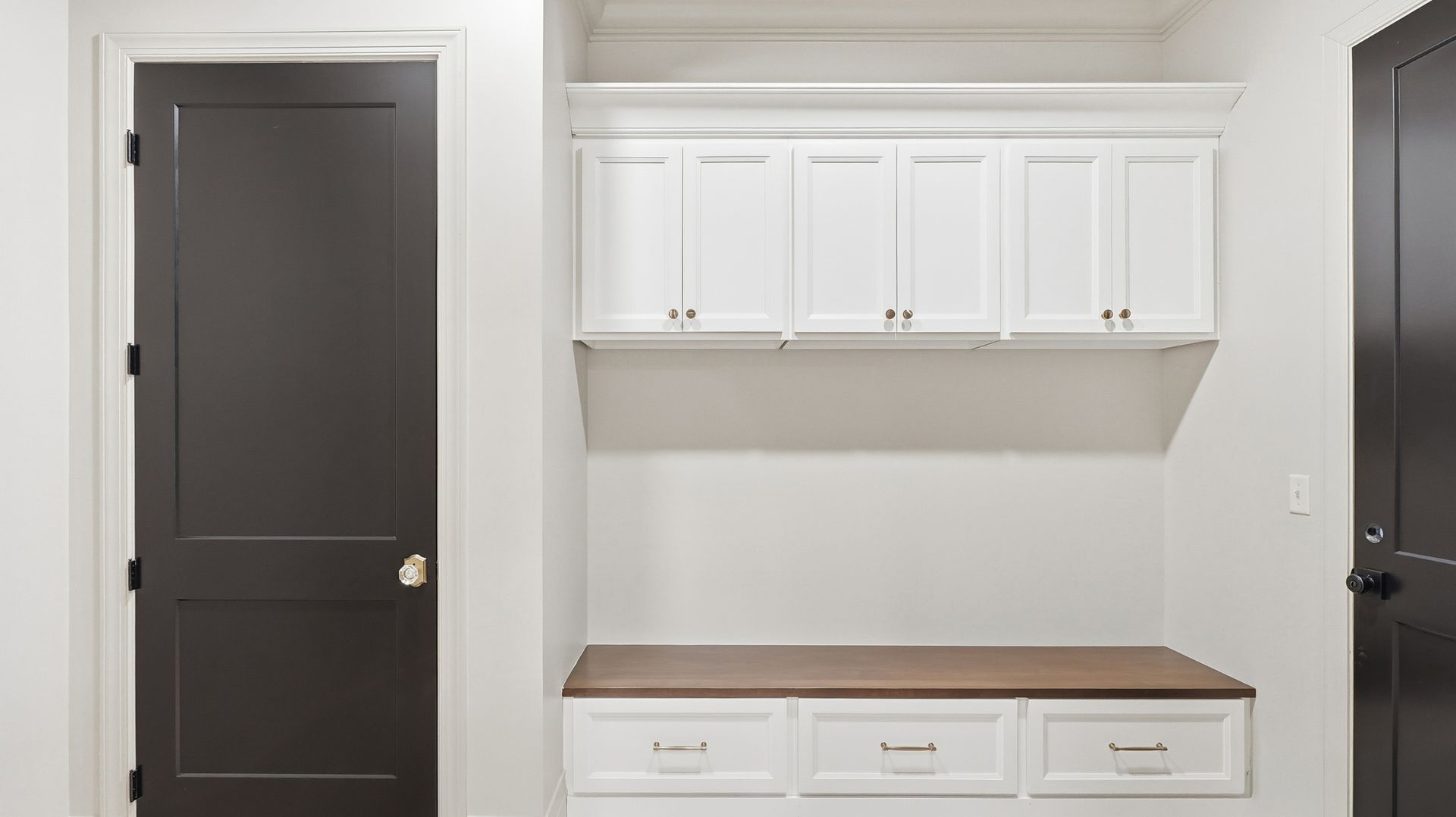 Mudroom with white cabinets, wood bench, and dark doors.
