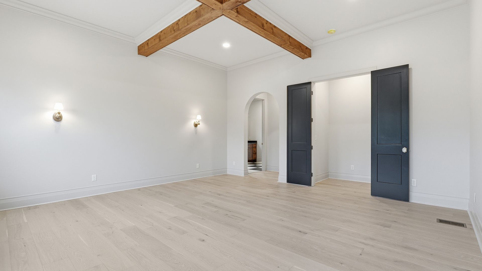 Empty white room with light wood floors, dark gray doors, and wooden beams on the ceiling.