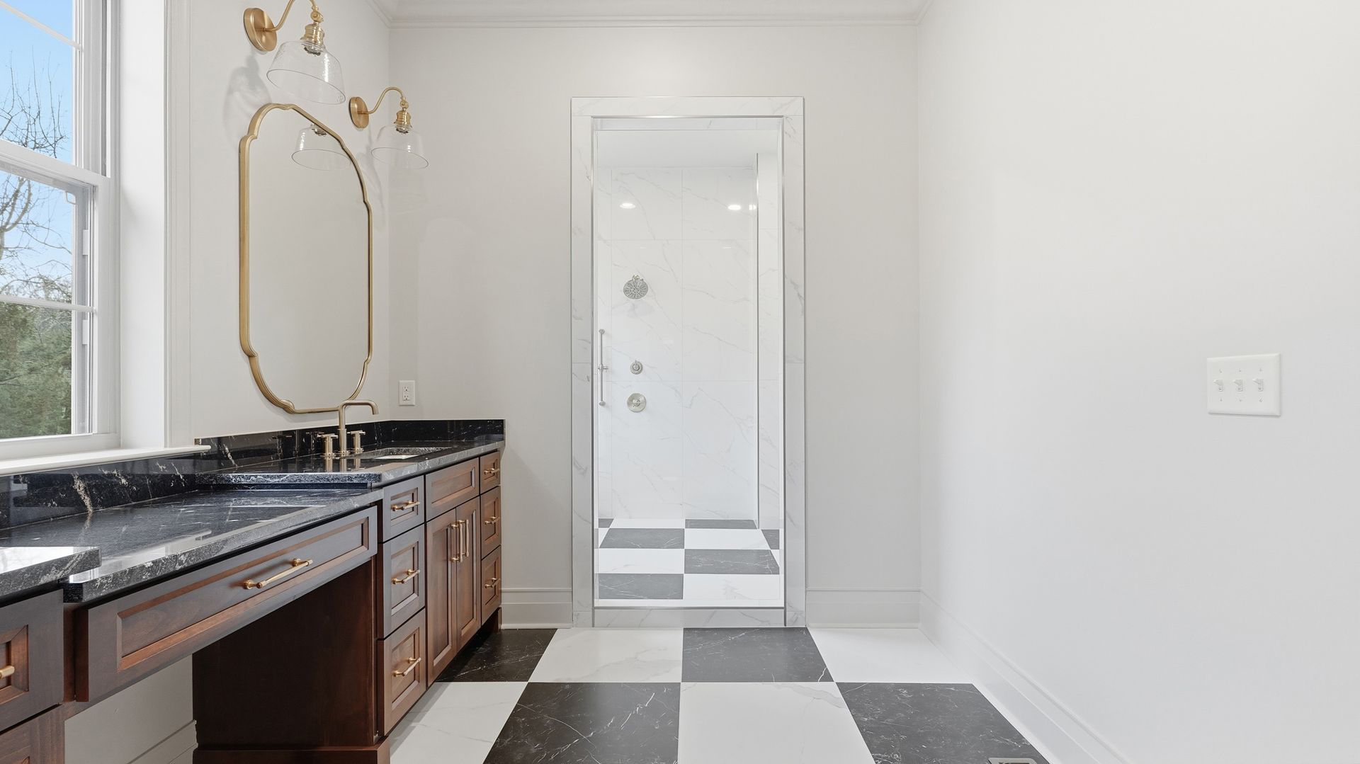 Bathroom with dark wood vanity, black countertop, gold mirror, and black and white checkered floor.