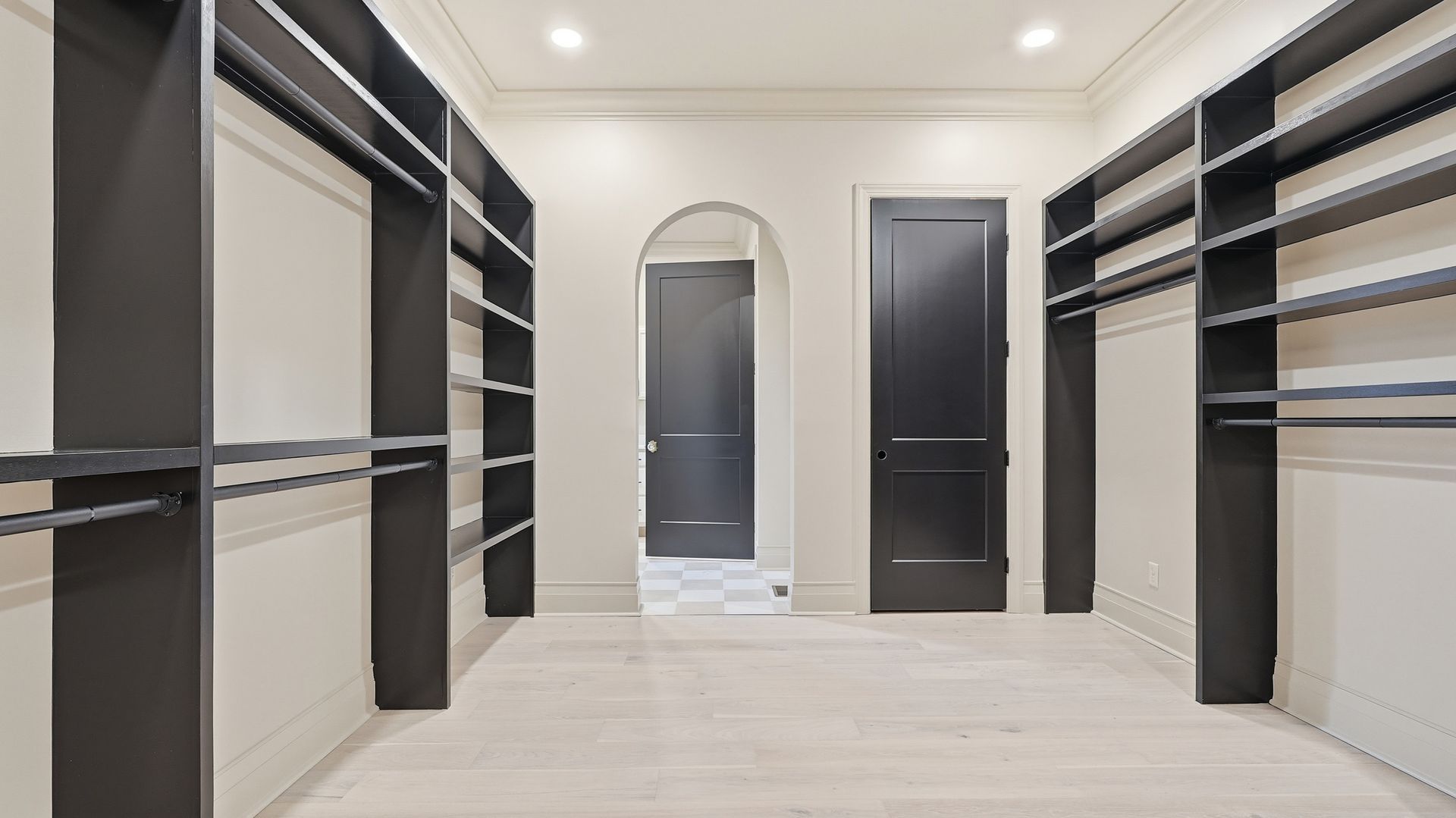 Empty walk-in closet with black shelves and rods, white walls and floor, and two black doors.