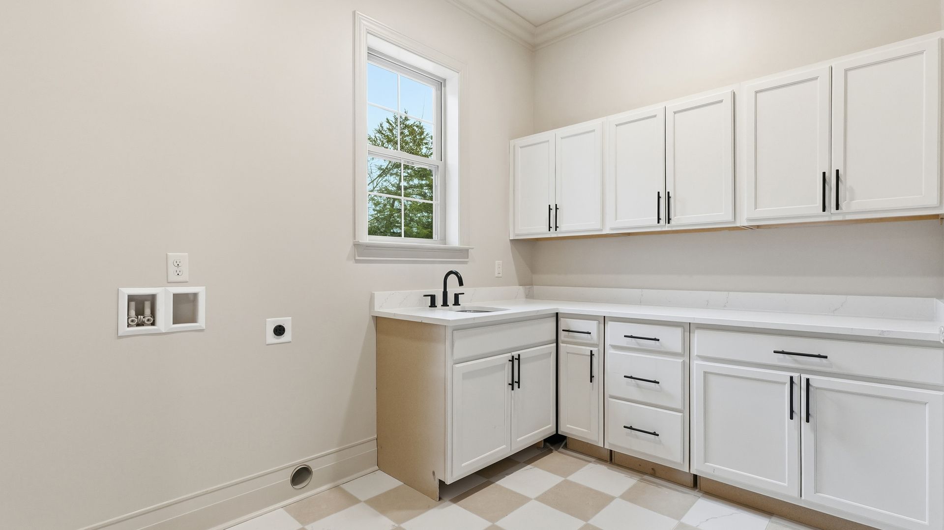 Laundry room with white cabinets, checkered floor, sink, and window.