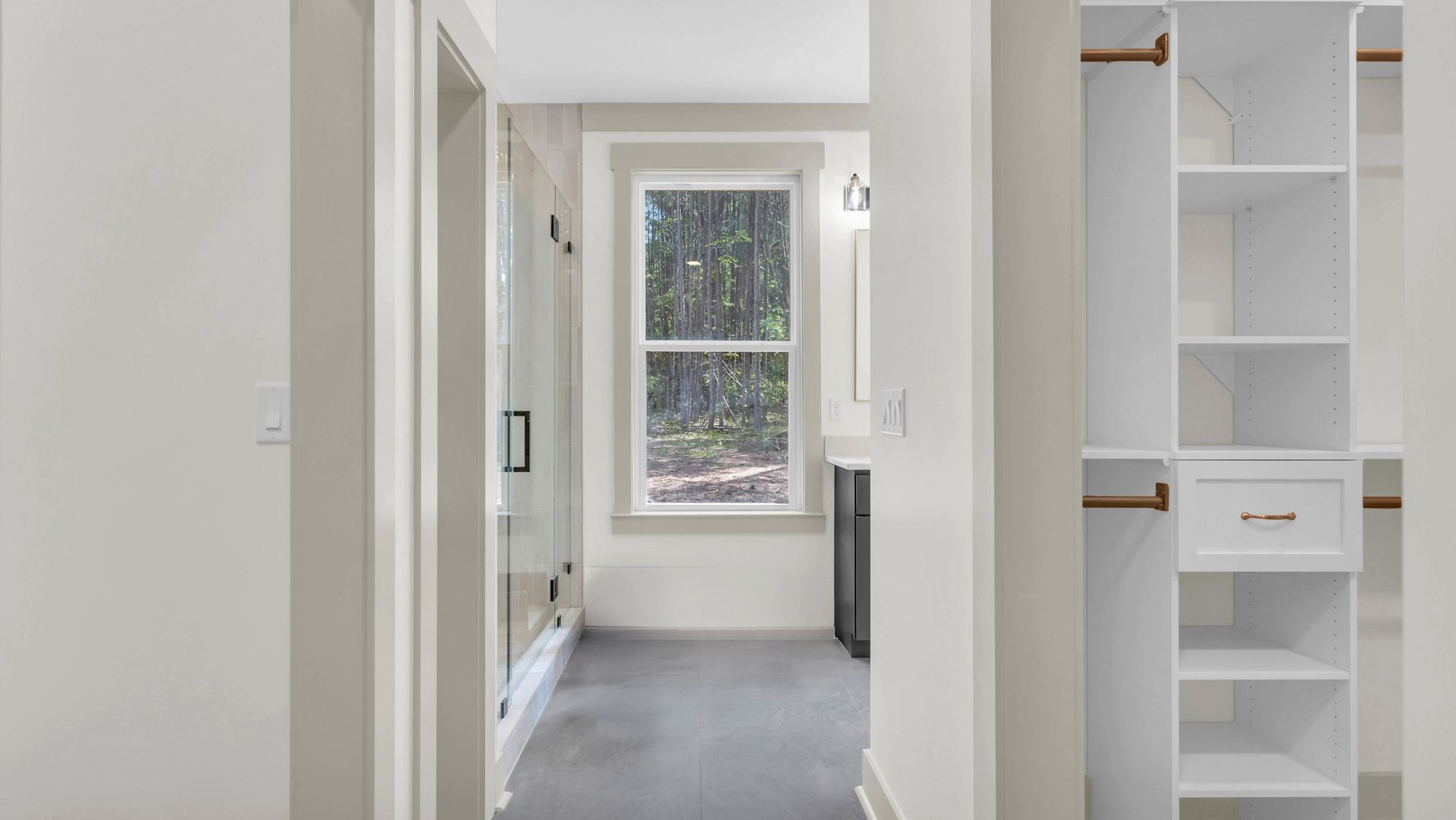 Hallway with white walls, a window overlooking trees, and a closet with shelves.