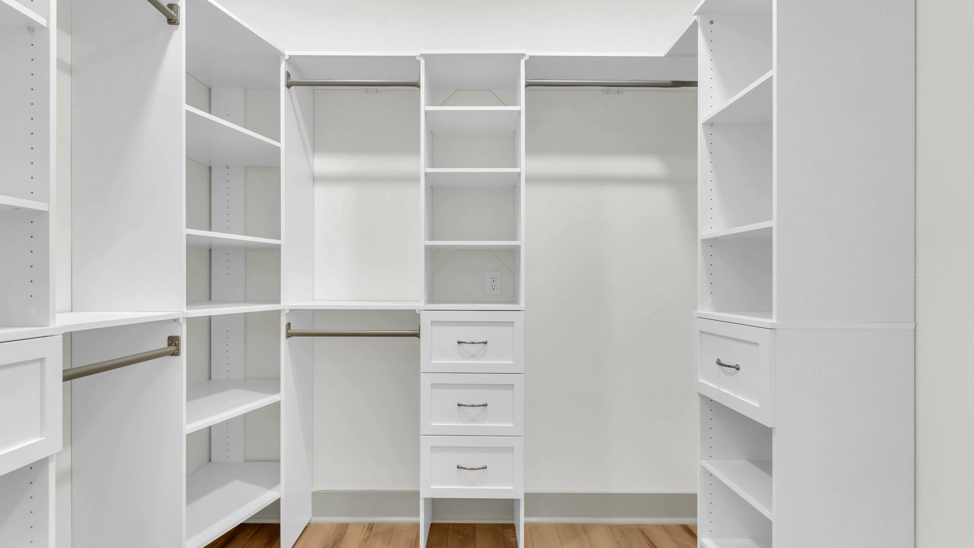 White walk-in closet with shelving, drawers, and hanging rods, against a light wood floor.