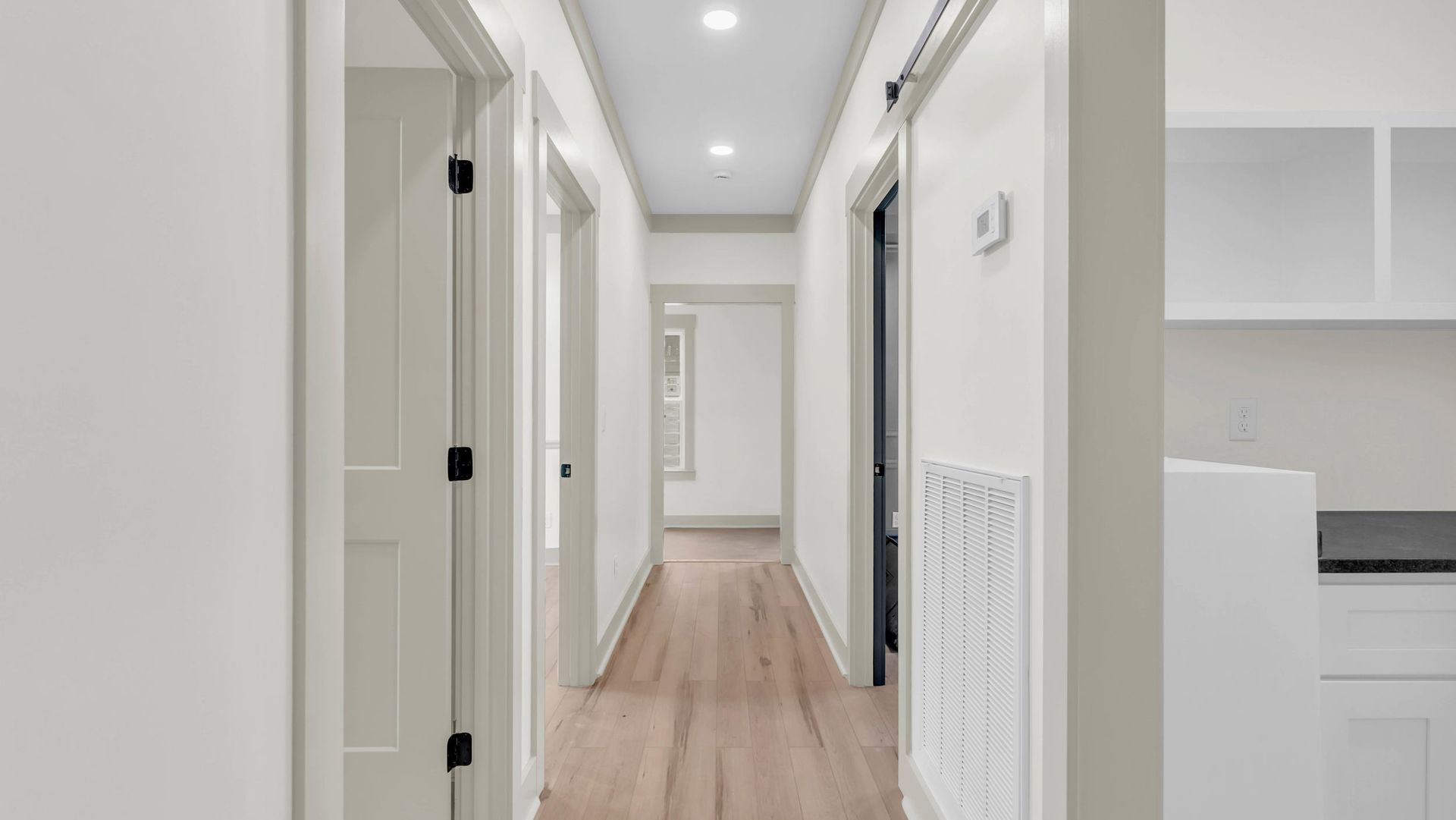 Narrow hallway with wood floors and white walls, doors, and trim.