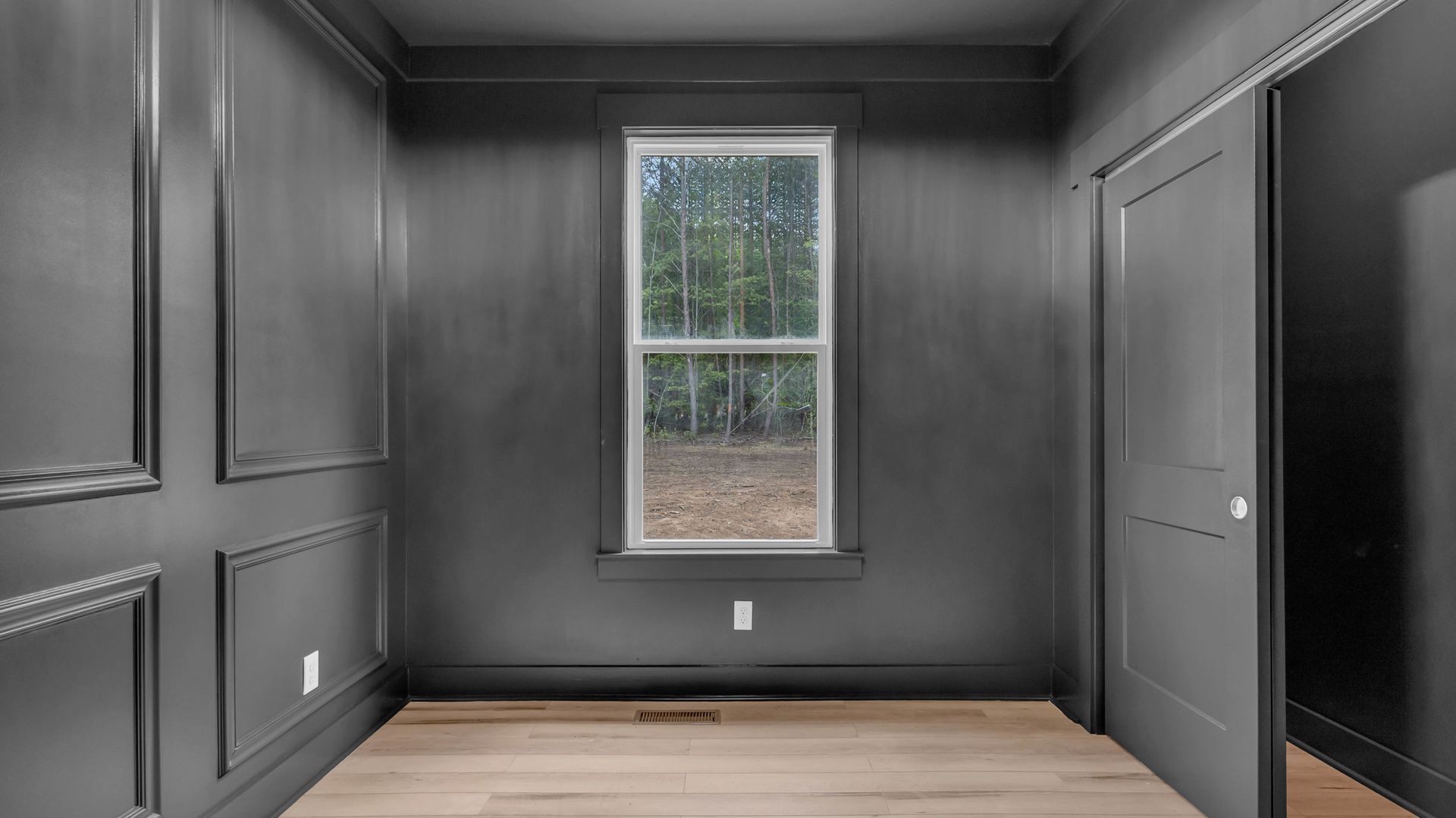 Empty room with dark gray walls, window, door, and light-colored wooden floor.