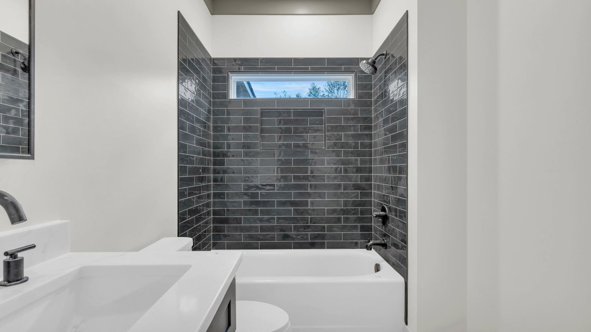 Bathroom with black tiled shower, white tub, sink, and toilet.