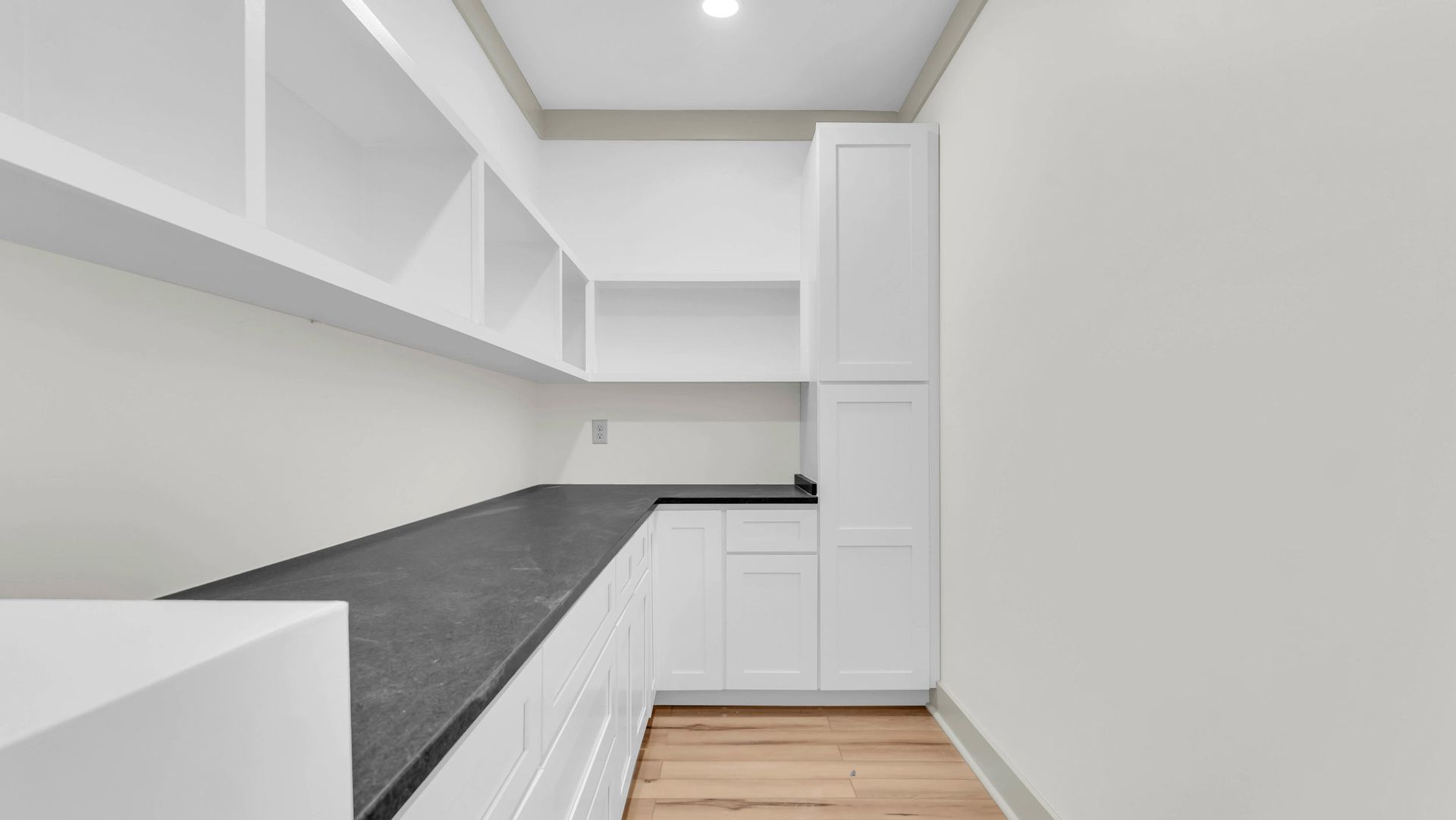 White pantry with shelves, cabinets, and a dark countertop.
