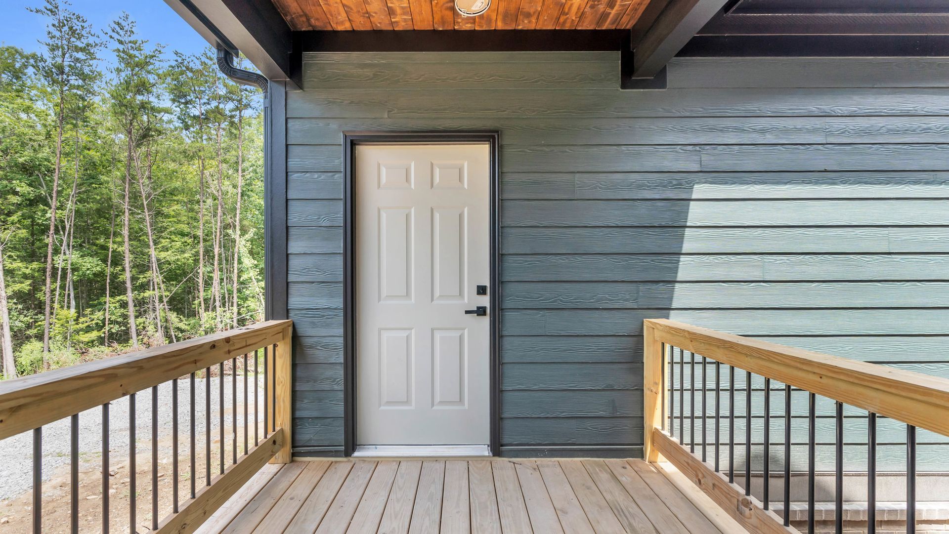 White door on a porch with wooden railing and grey siding.