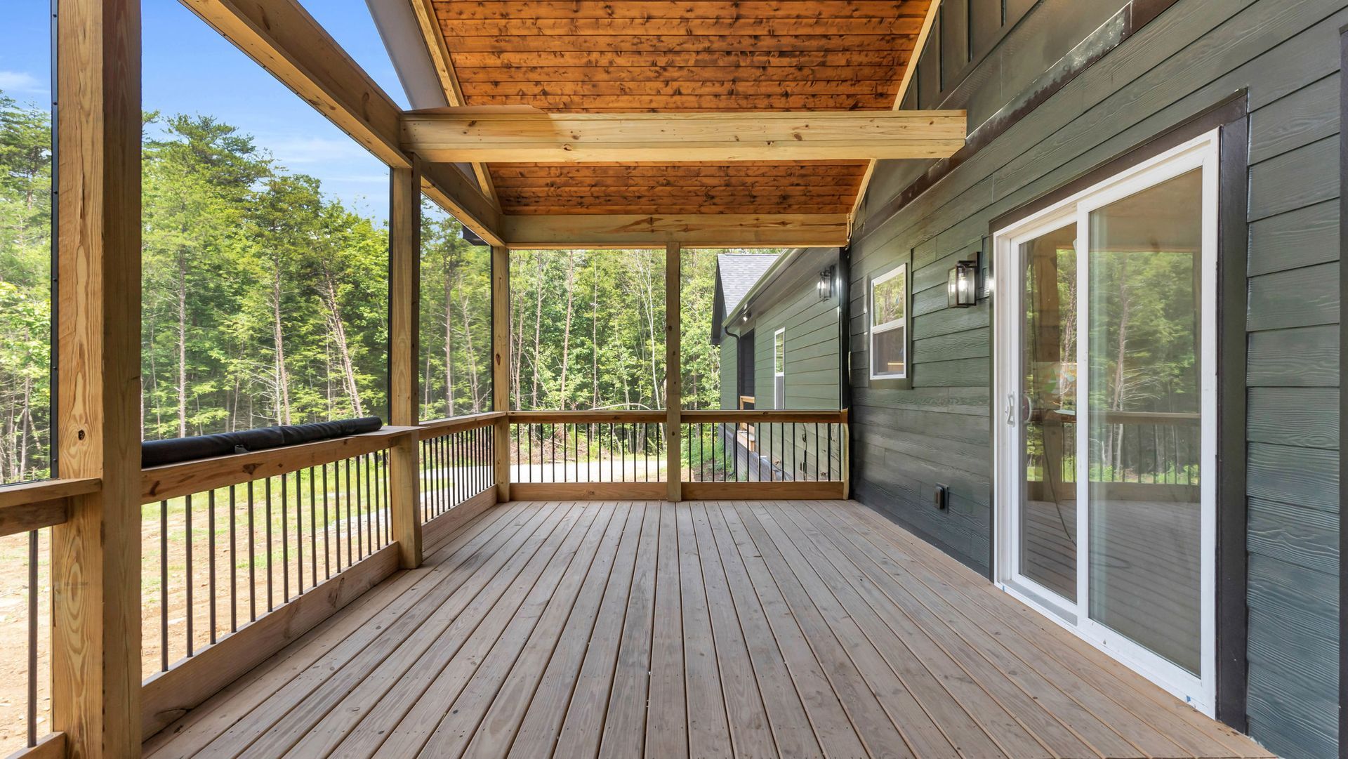 Covered wooden porch with screen and railing, attached to a dark green house.