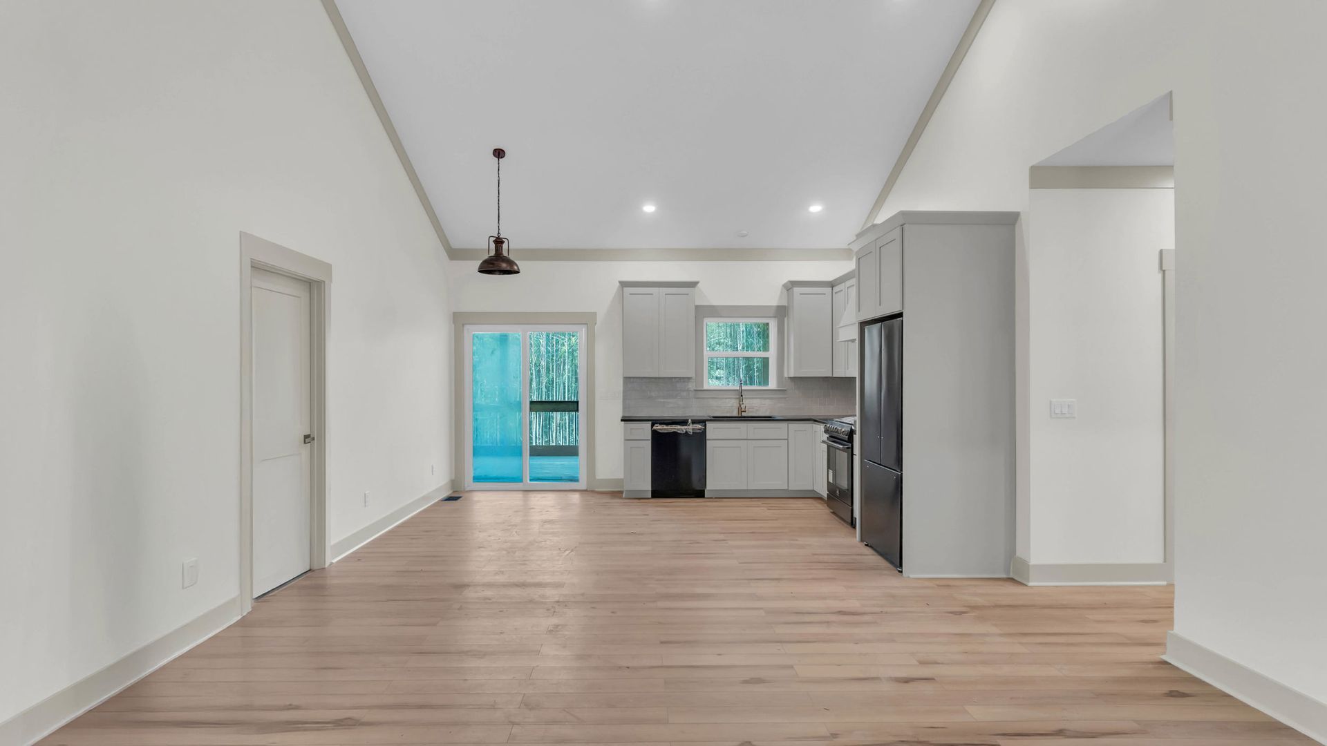Open-concept living space with kitchen, light wood floors, white walls, and access to a balcony.