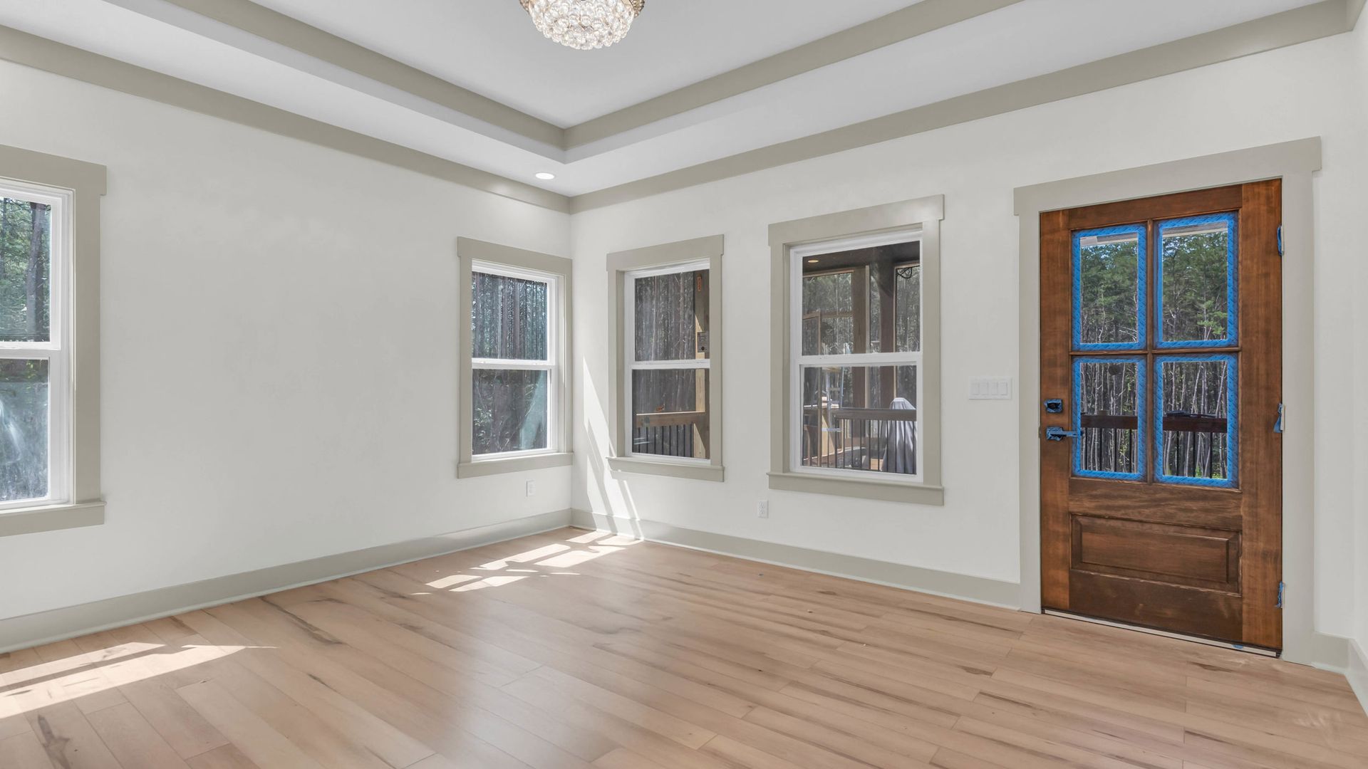 Empty room with wood floors, white walls, and windows; a wooden door is on the right.