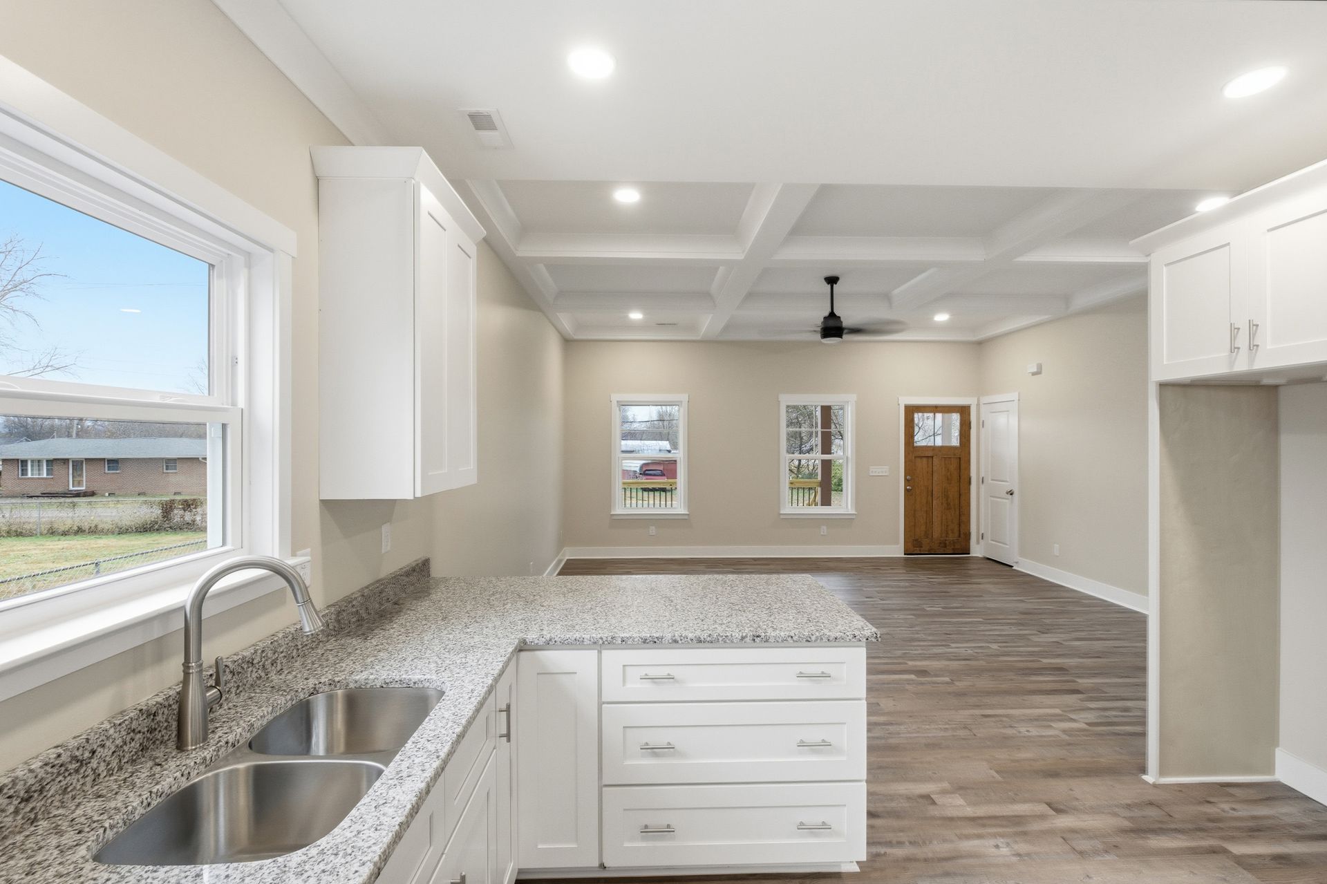 Kitchen with white cabinets, granite countertop, stainless steel sink, and light wooden floor.
