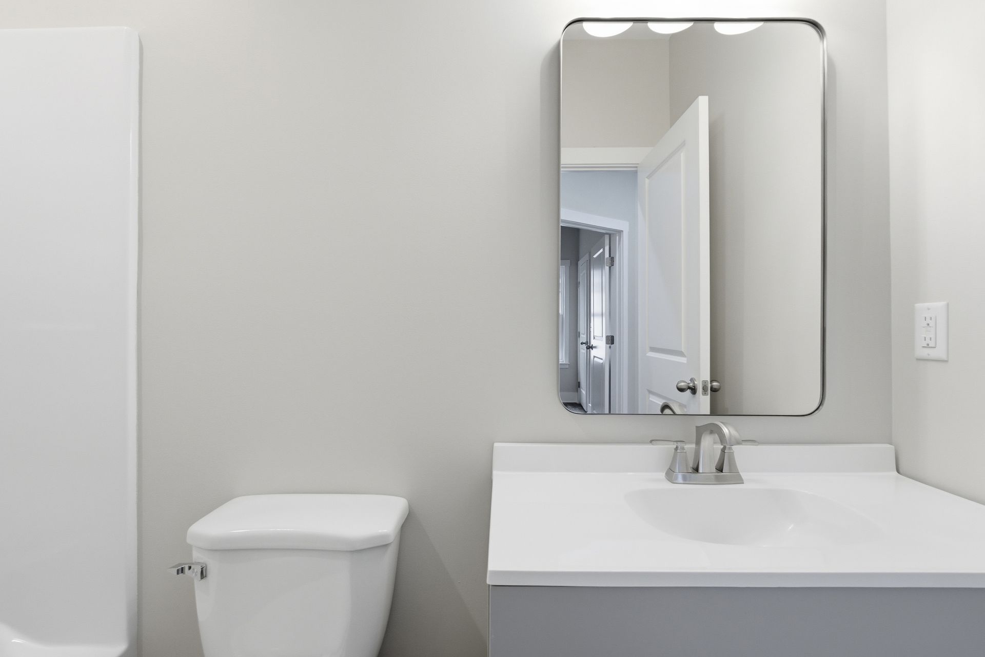 Bathroom with a toilet, sink, and mirror; gray walls, white countertop, and open door reflection.