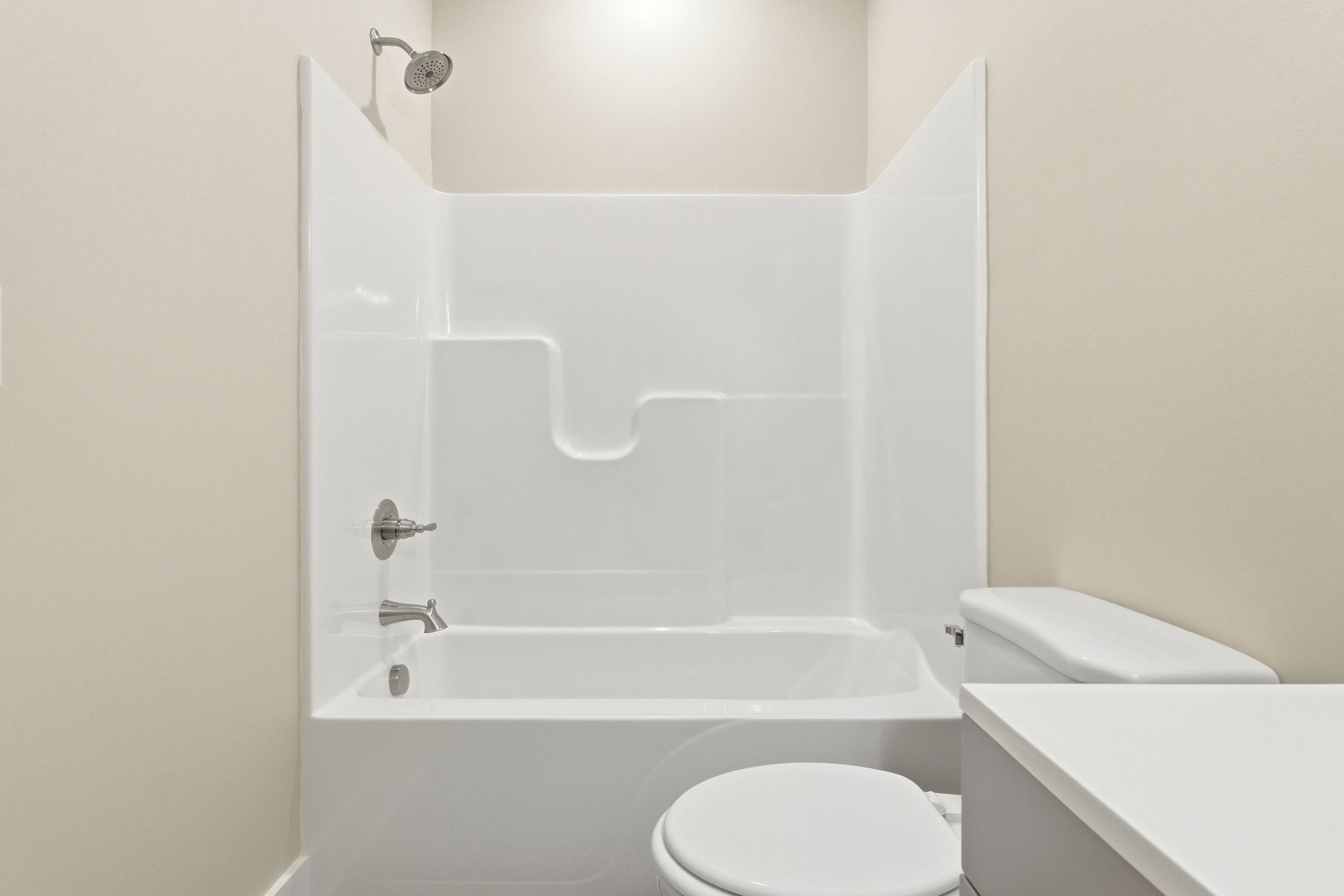 White bathroom with tub, toilet, and showerhead against beige walls.