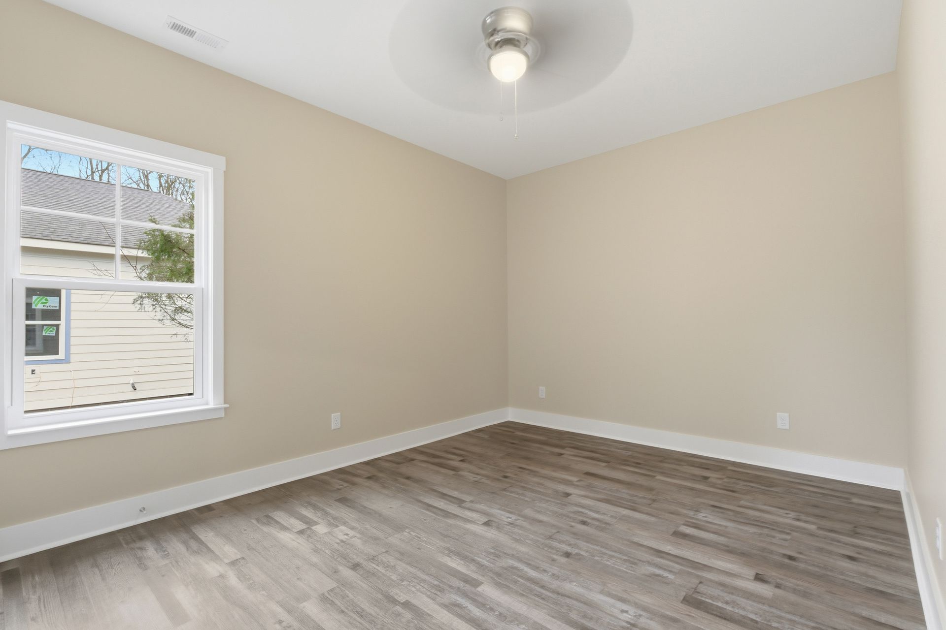 Empty room with wood-look flooring, beige walls, white trim, and a window. Ceiling fan centered overhead.