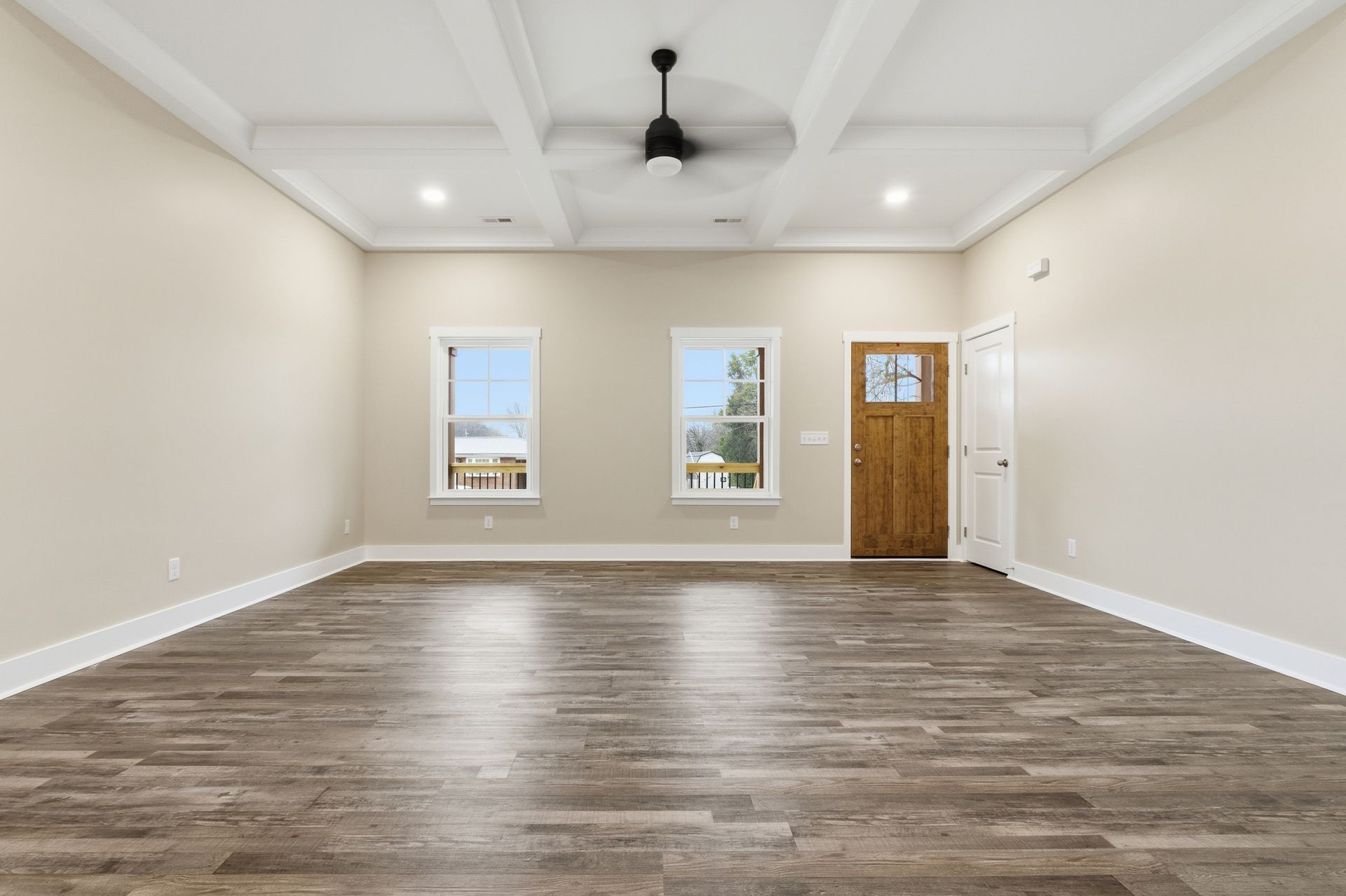 Empty room with wood-look flooring, beige walls, two windows, and a wooden door.
