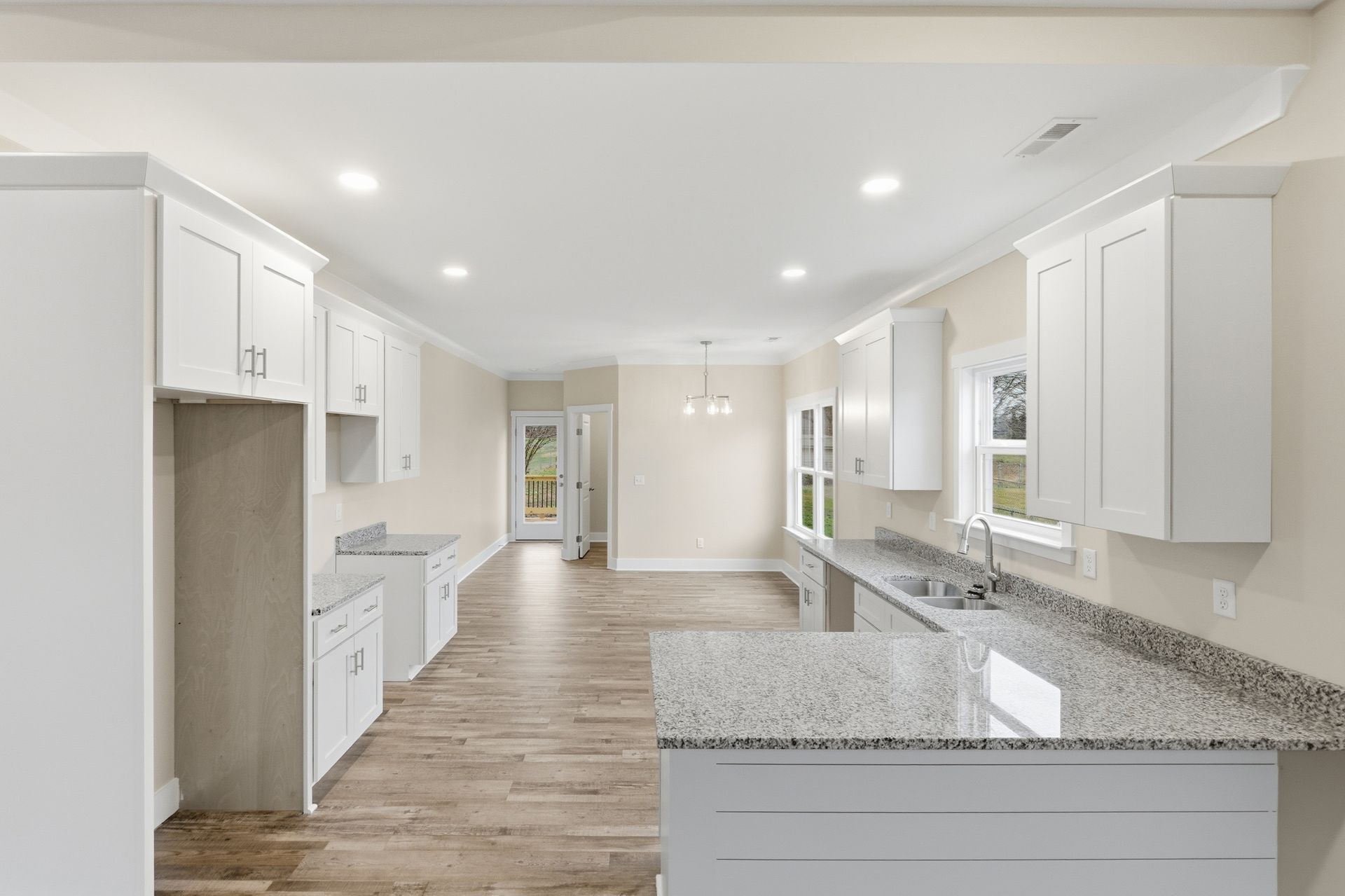 Kitchen with white cabinets, granite countertops, and light wood-look flooring. Leads to an open dining area and a door.