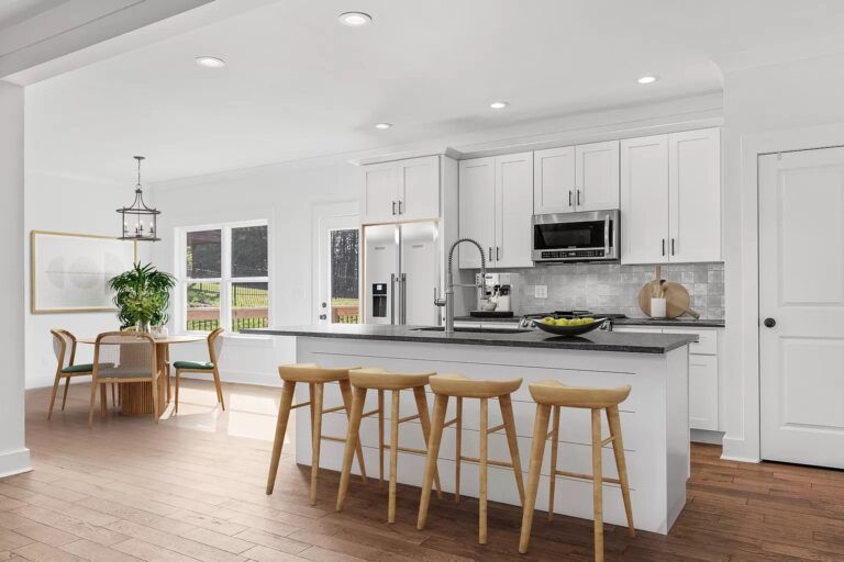 A kitchen with white cabinets and stools and a large island in the middle.