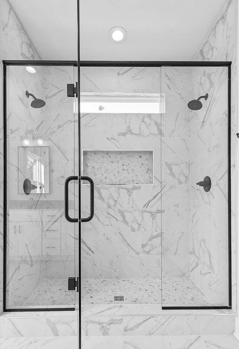A black and white photo of a bathroom with a walk in shower.