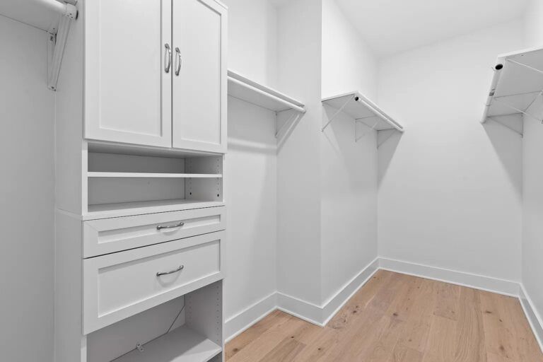 A walk in closet with hardwood floors and white cabinets.