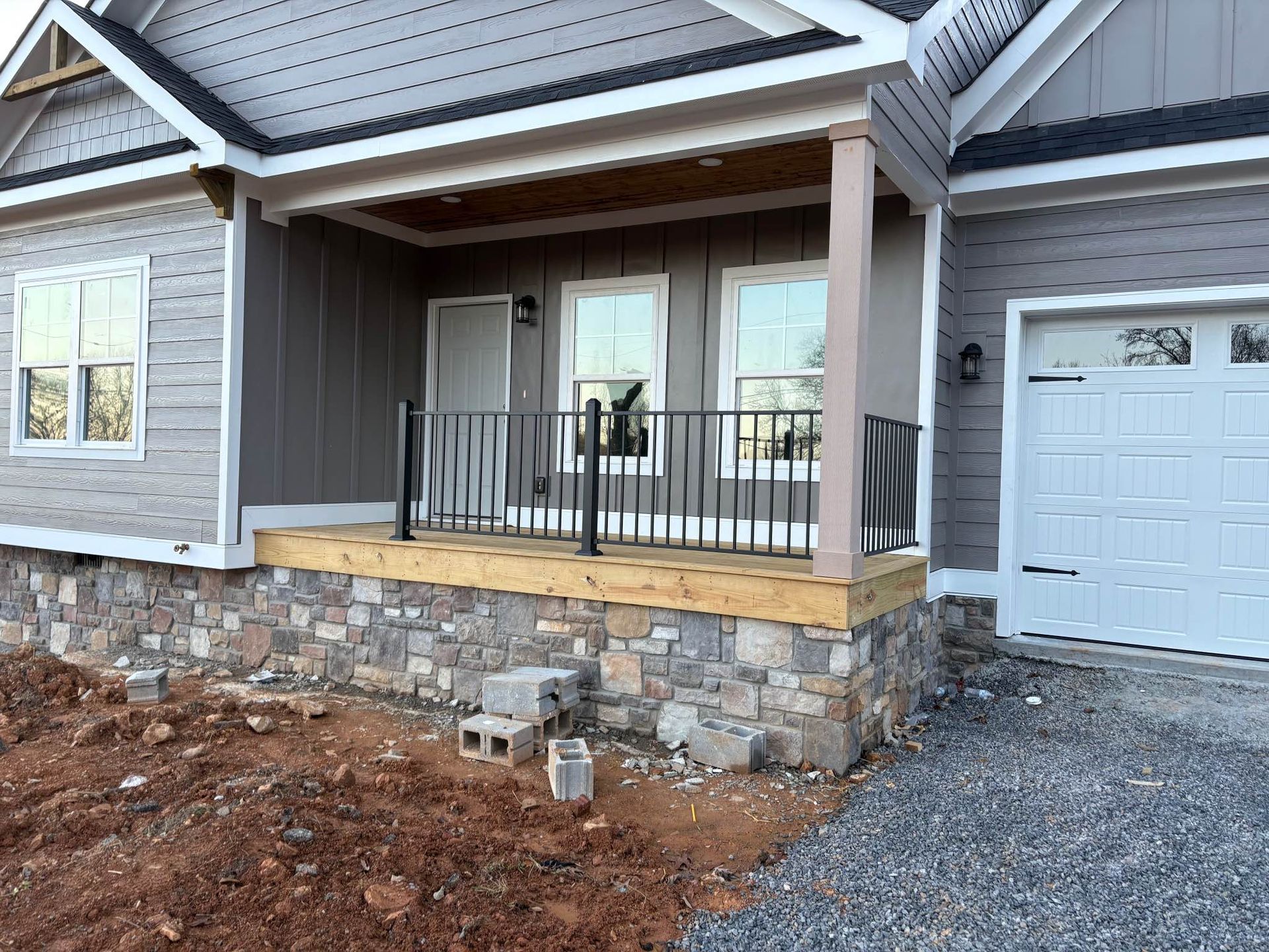 A house with a porch and a garage under construction.