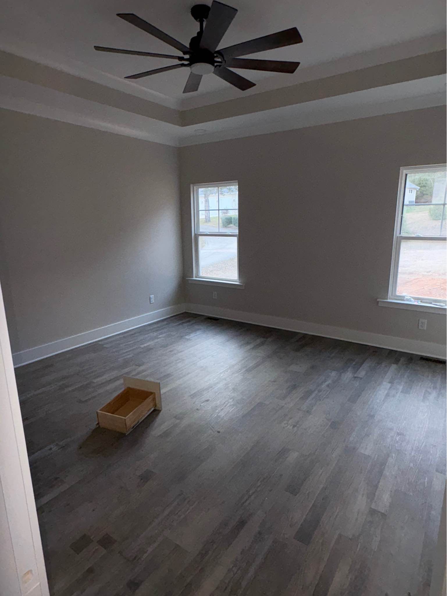 An empty room with a ceiling fan and two windows.