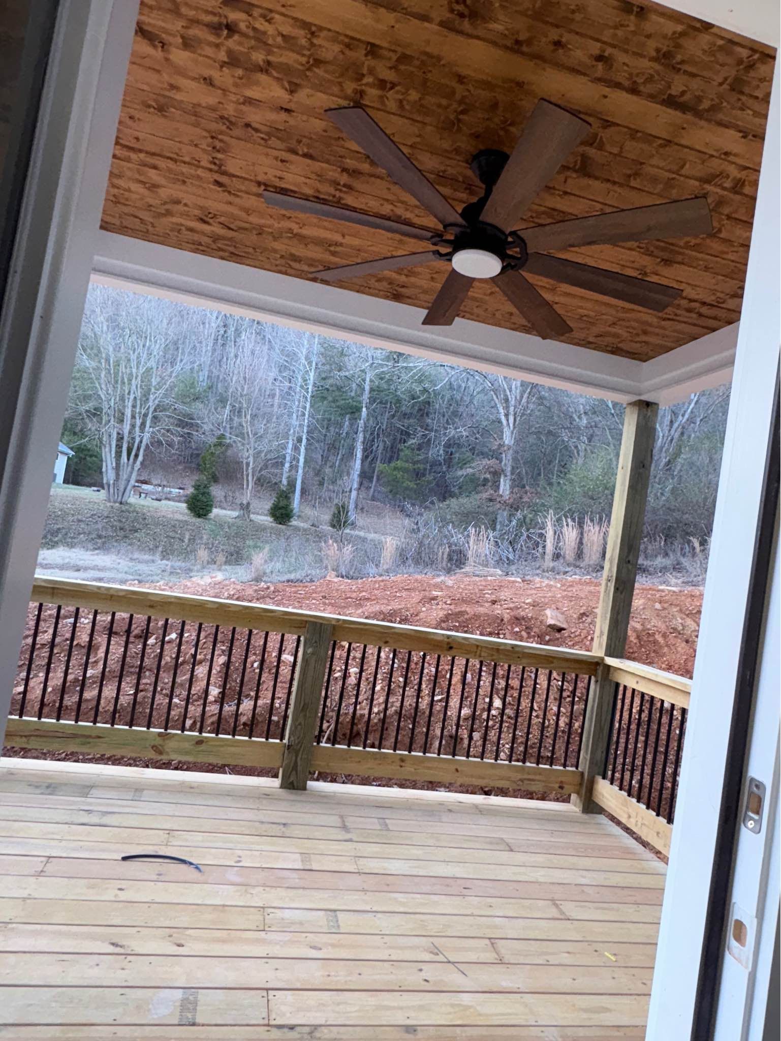 A porch with a ceiling fan and a view of a forest.